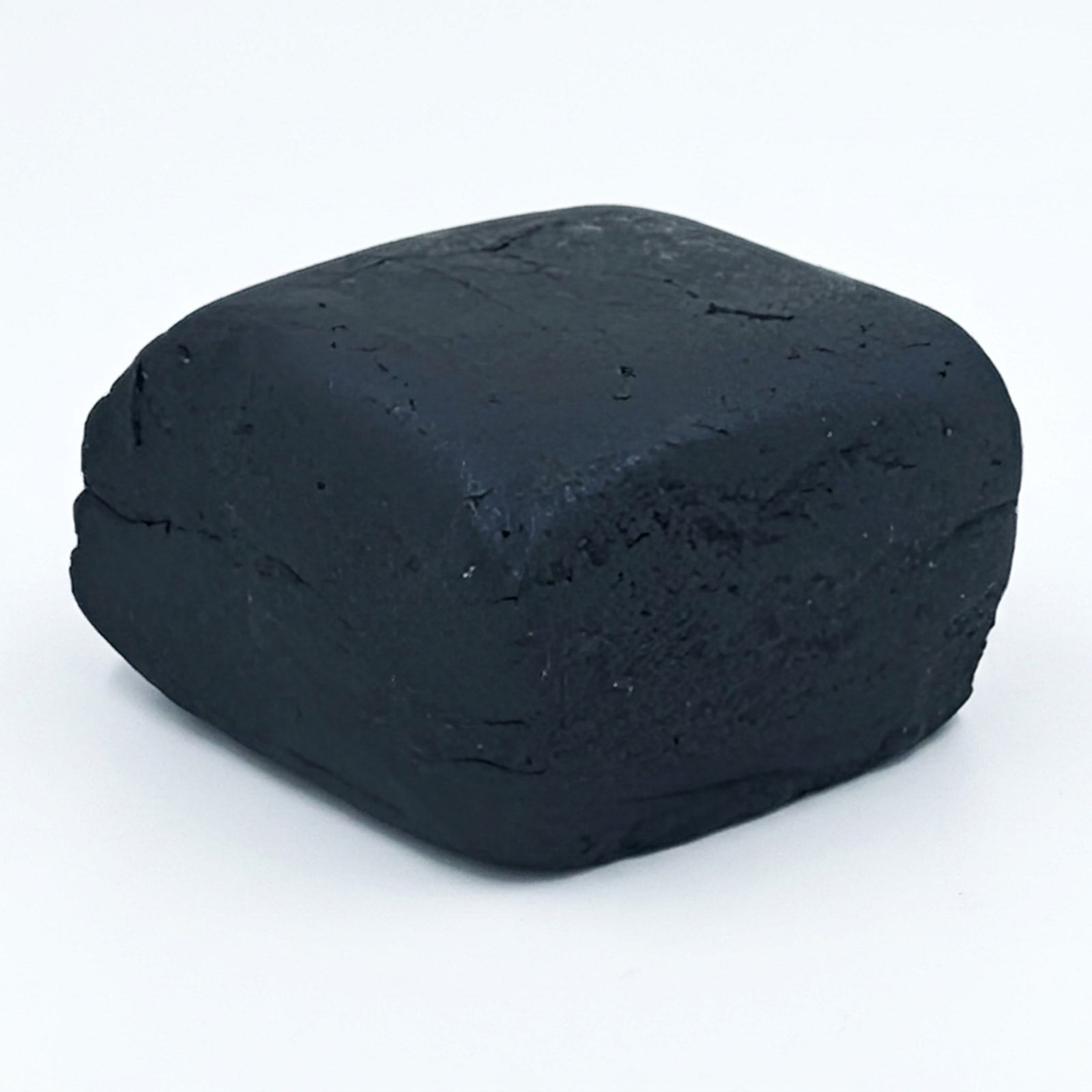A pressed block of black hash photographed on a white background, its rounded edges and surface cracks visible.