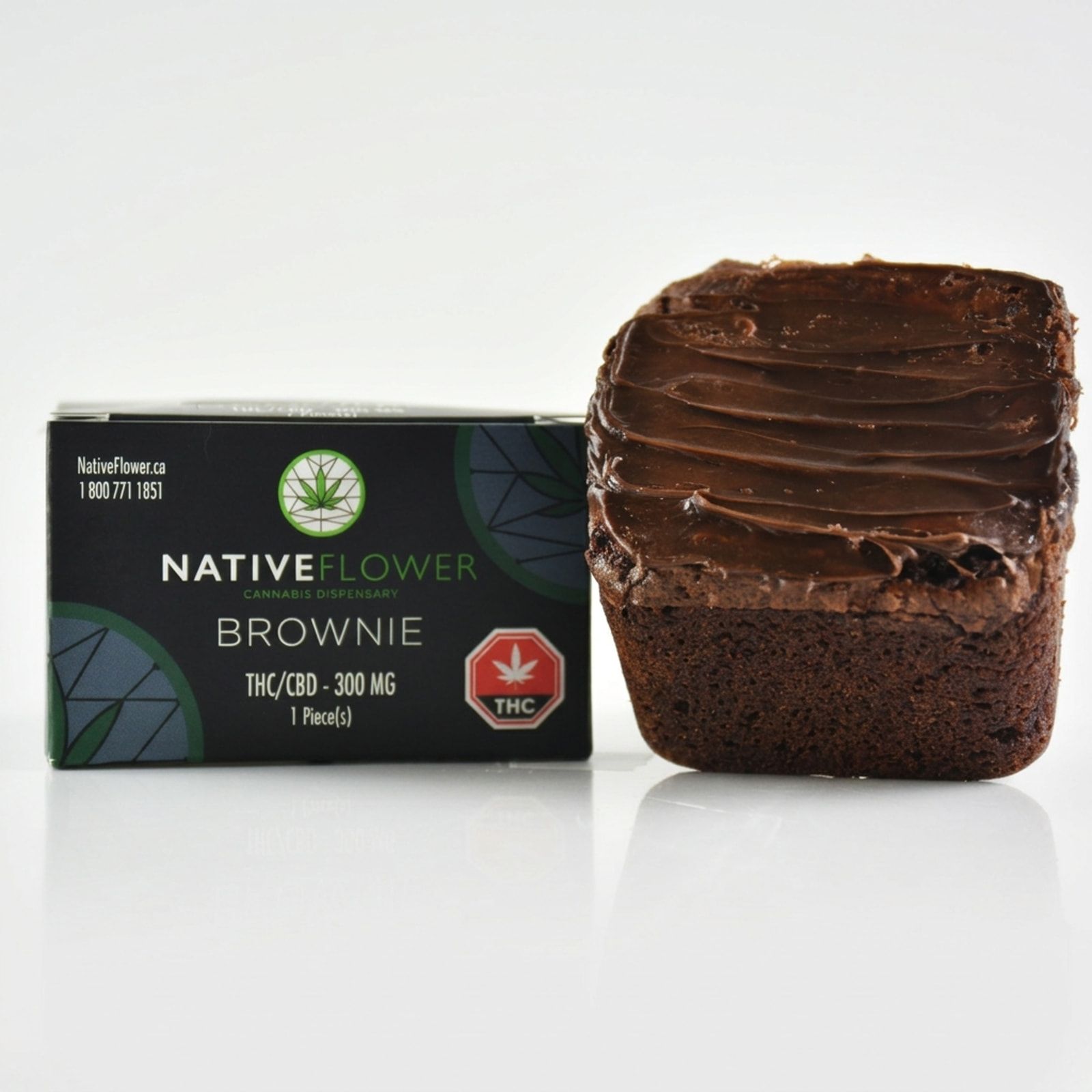 A frosted Native Flower brownie standing beside its black box on a white background.