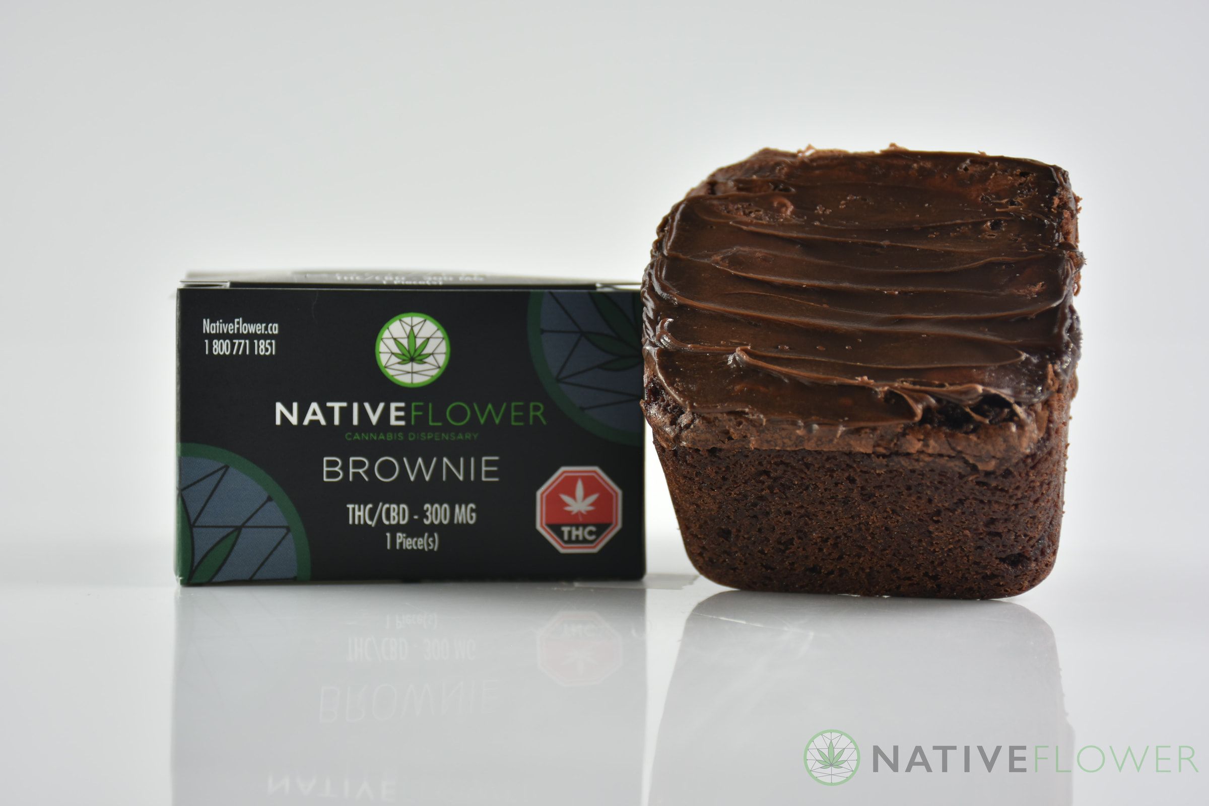 A thickly frosted Native Flower brownie beside its black carton.