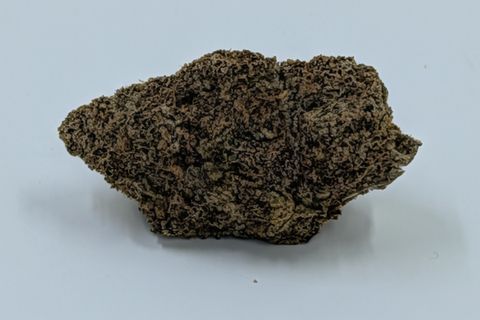 A cured bud of Cake & Bake, brown and densely frosted, much wider than it is tall, photographed against a plain pale-grey background.