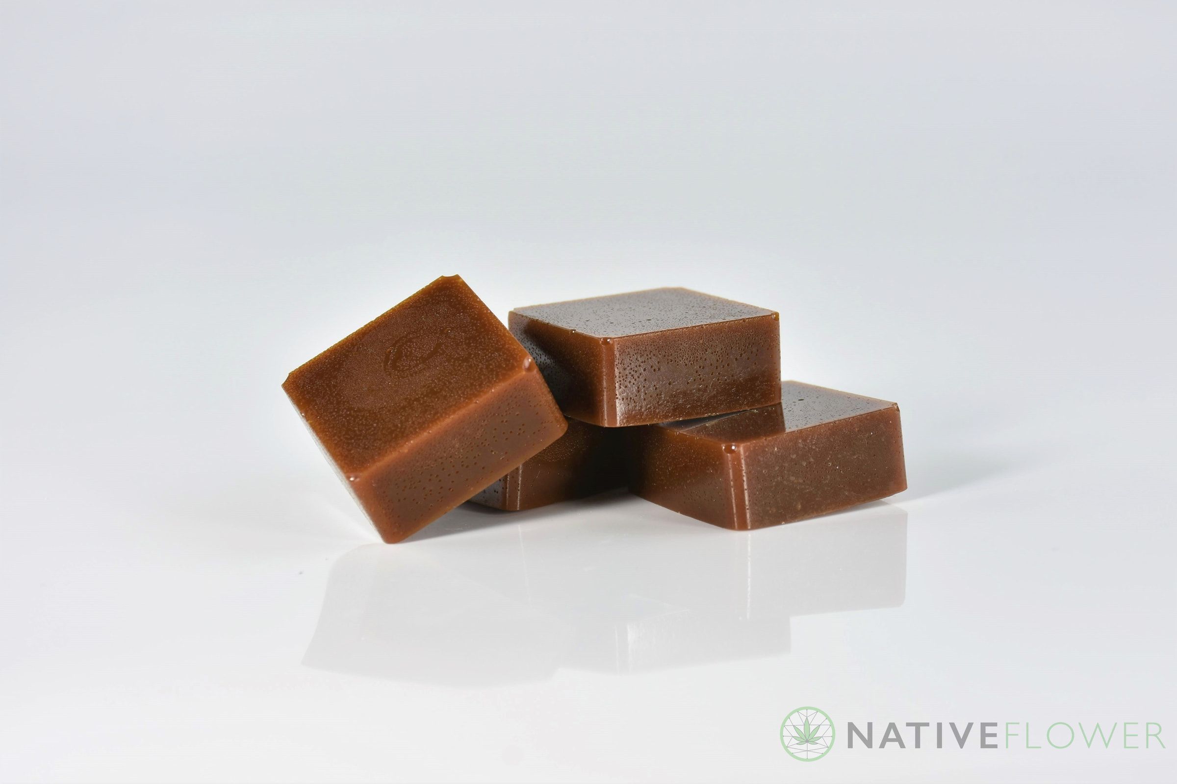 Four amber toffee squares stacked loosely on a white surface.
