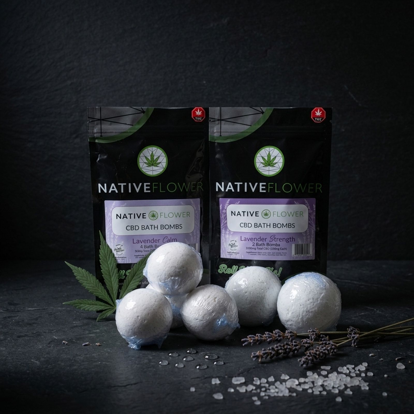 Two Native Flower CBD bath bomb pouches with lilac labels behind six white bath bombs, with lavender sprigs, coarse salt and a cannabis leaf.