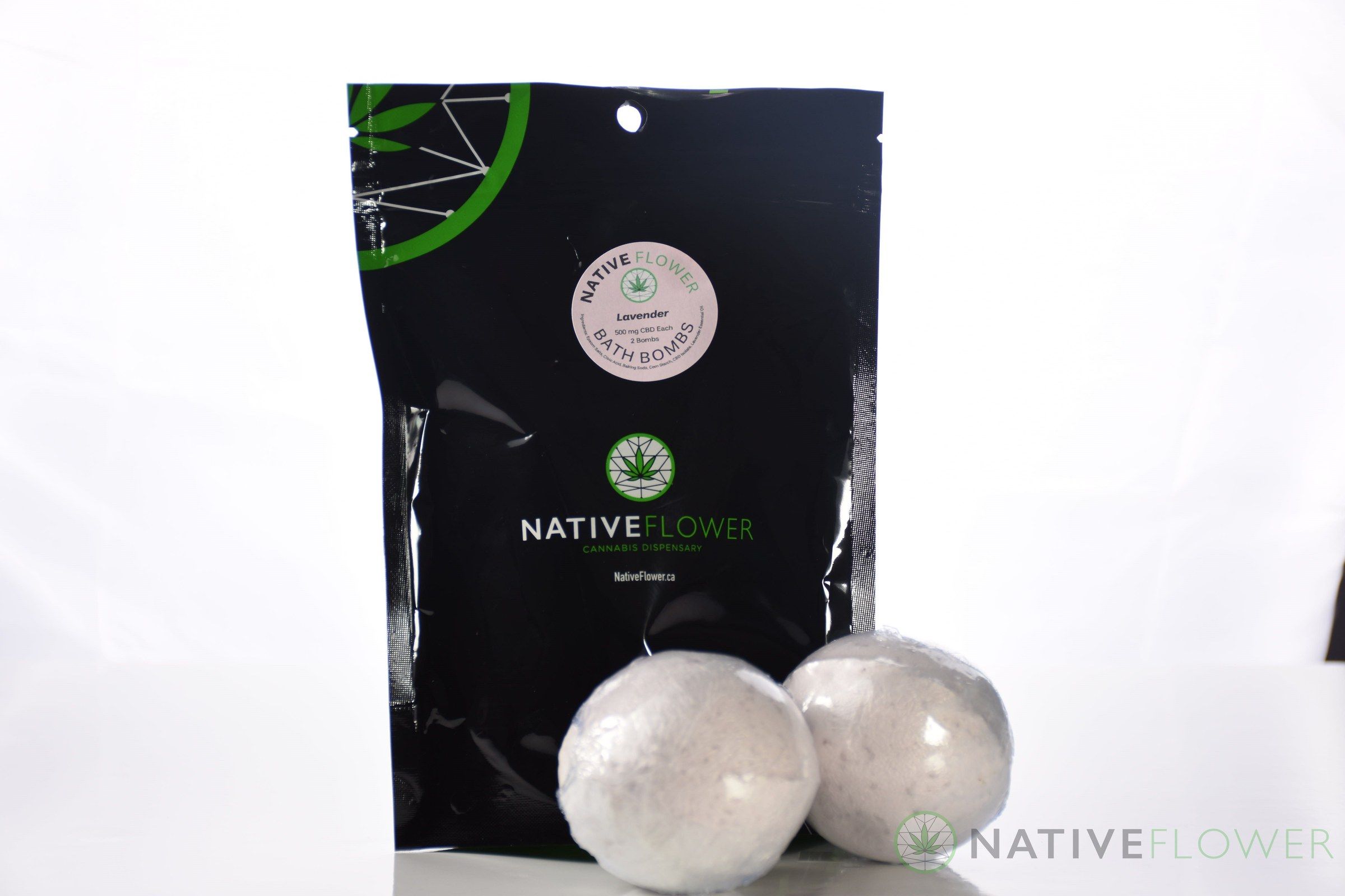 A black Native Flower bath bomb pouch labelled Lavender, with two white bath bombs resting in front of it.