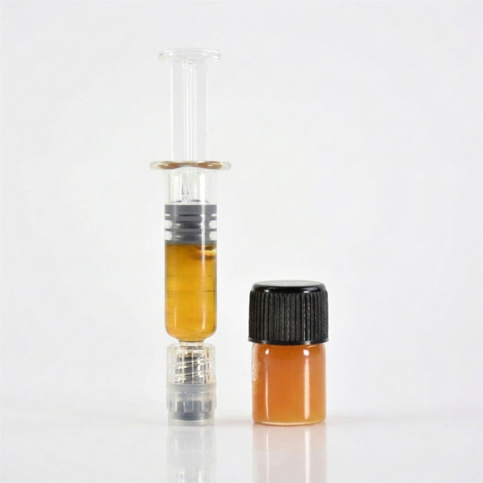 A glass syringe of amber CBD oil standing beside a small vial with a black cap, on a white background.