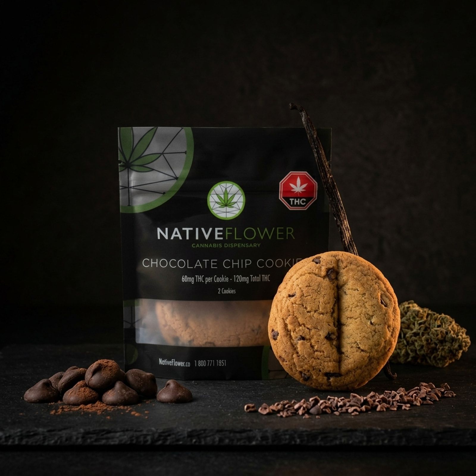 A chocolate chip cookie leaning against its black Native Flower pouch on slate, with chocolate chips, cacao nibs and a cannabis bud.