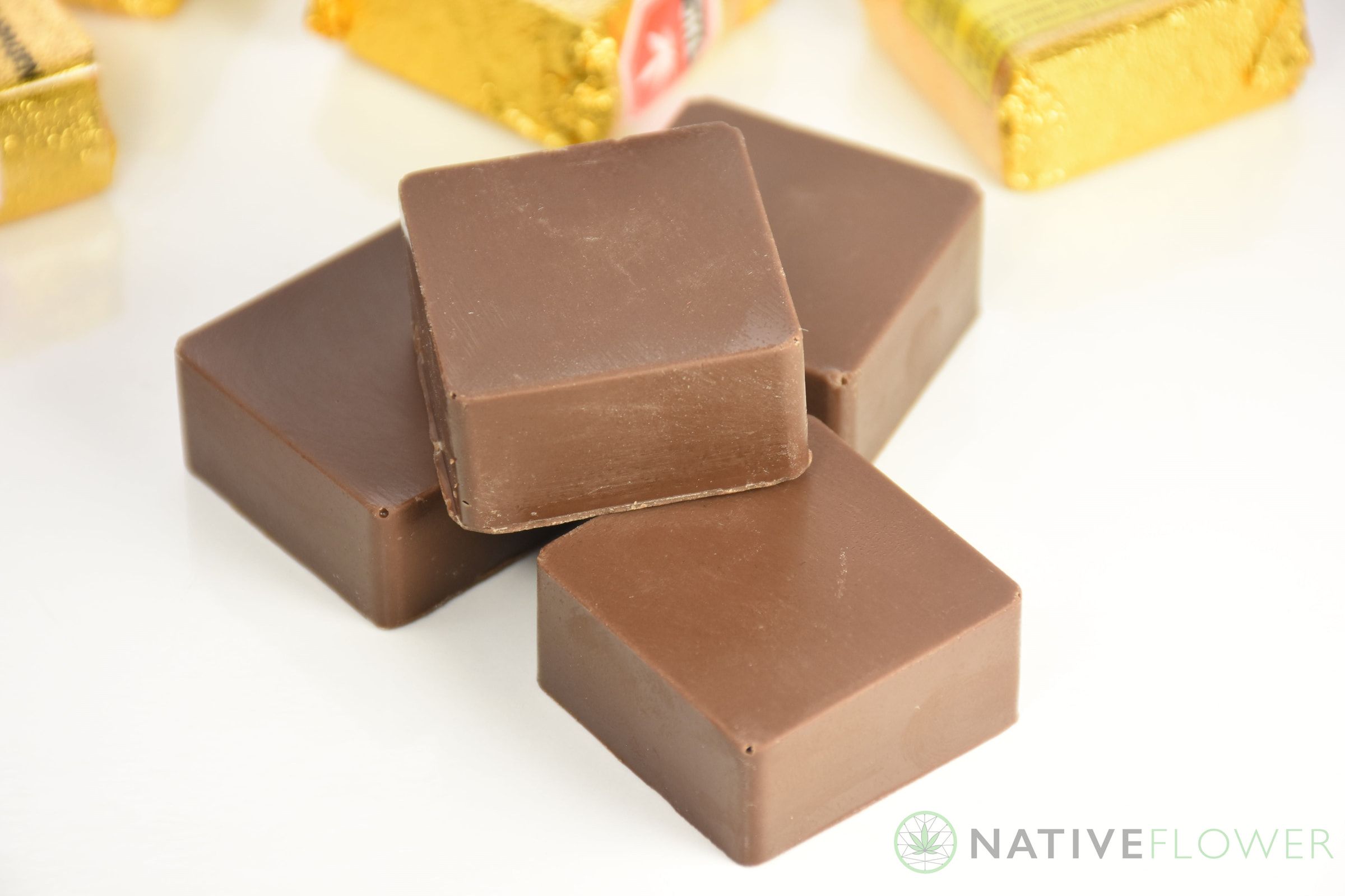 Four milk chocolate squares stacked loosely, gold foil wrappers behind them.