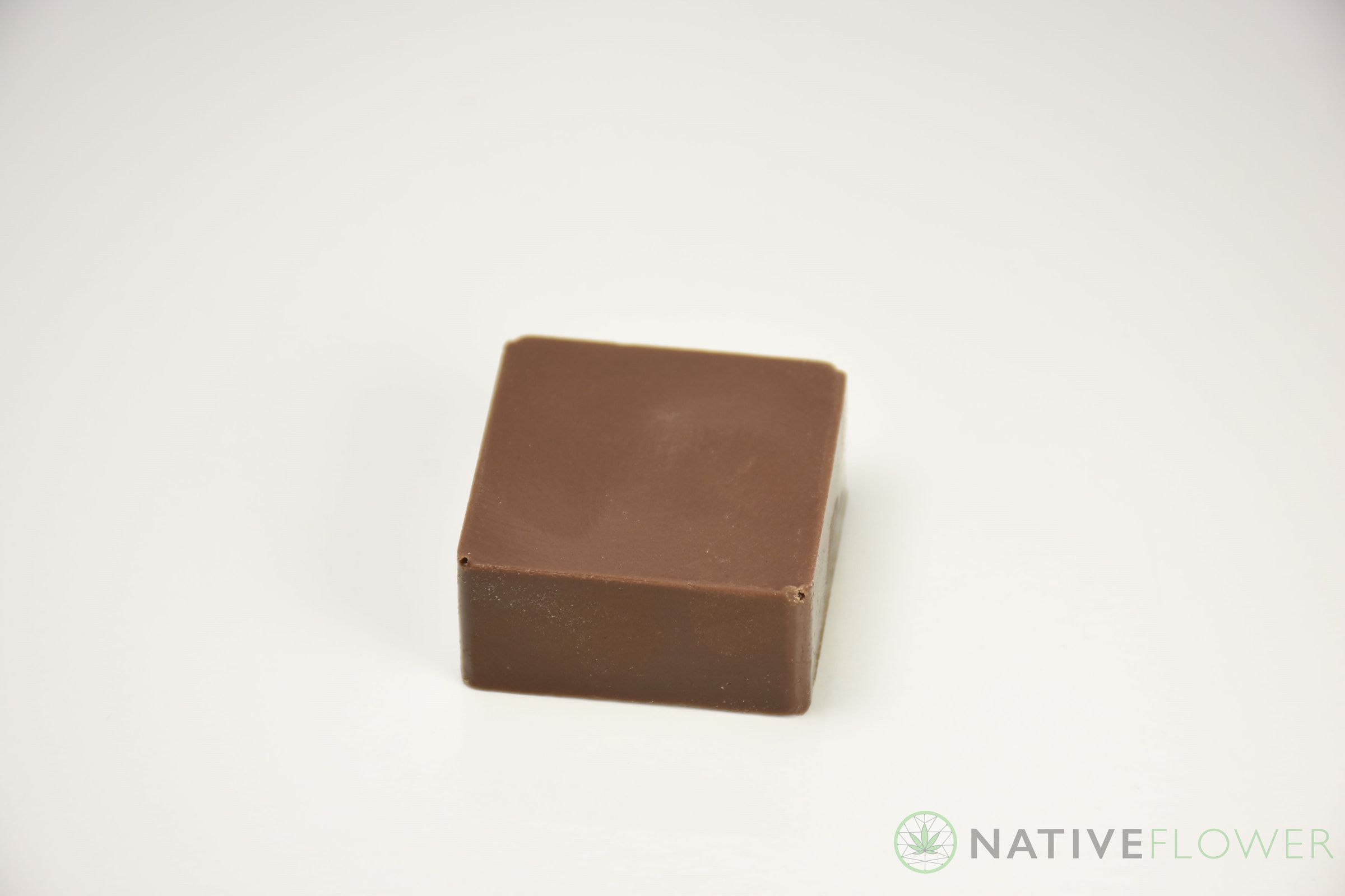 A single milk chocolate square photographed on a white surface.