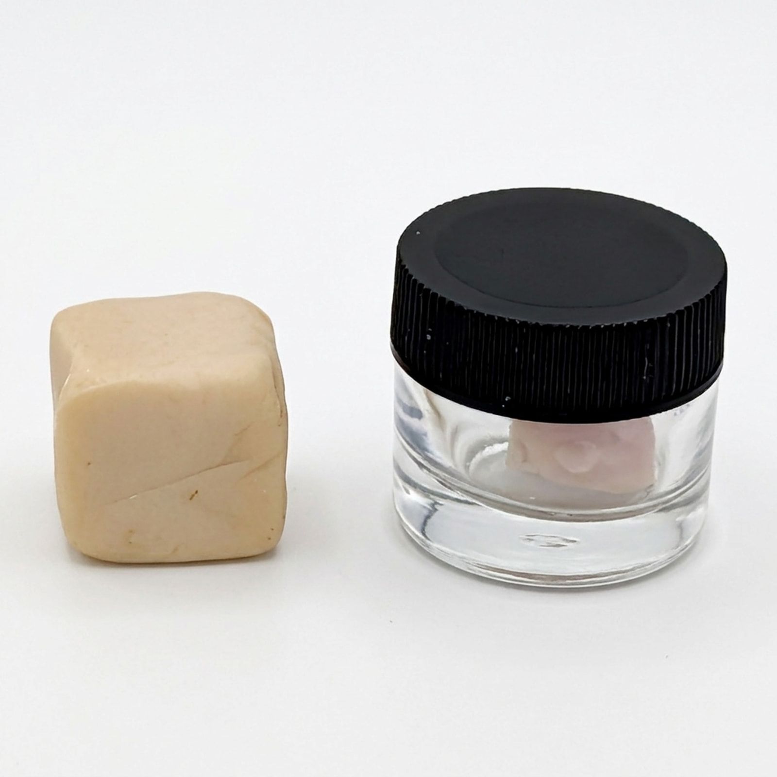 A pale cube of diamond hash beside a lidded glass jar holding a pale pink piece, on a white background.