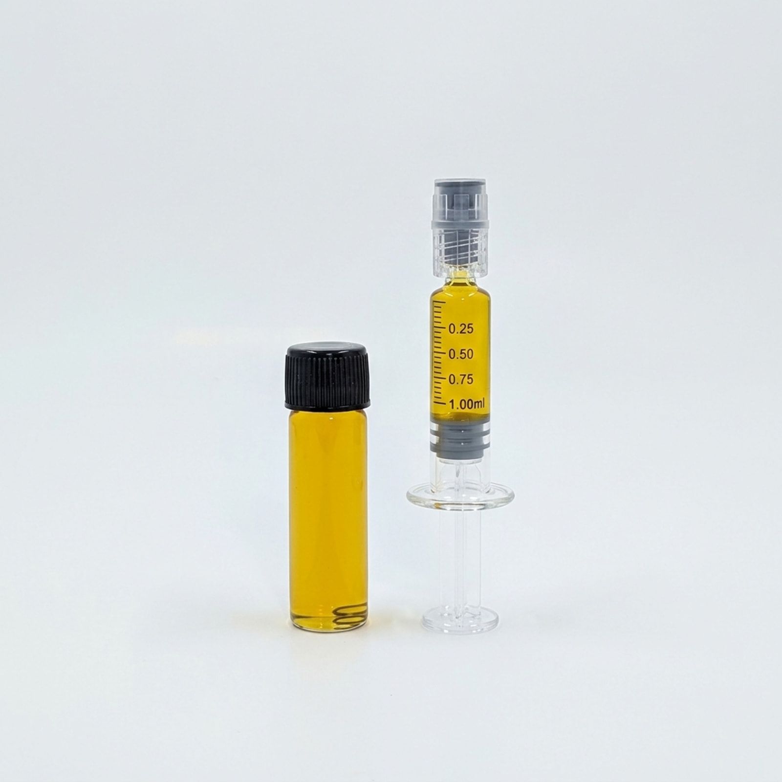 A capped glass vial of golden distillate beside a filled syringe, photographed on a white background.