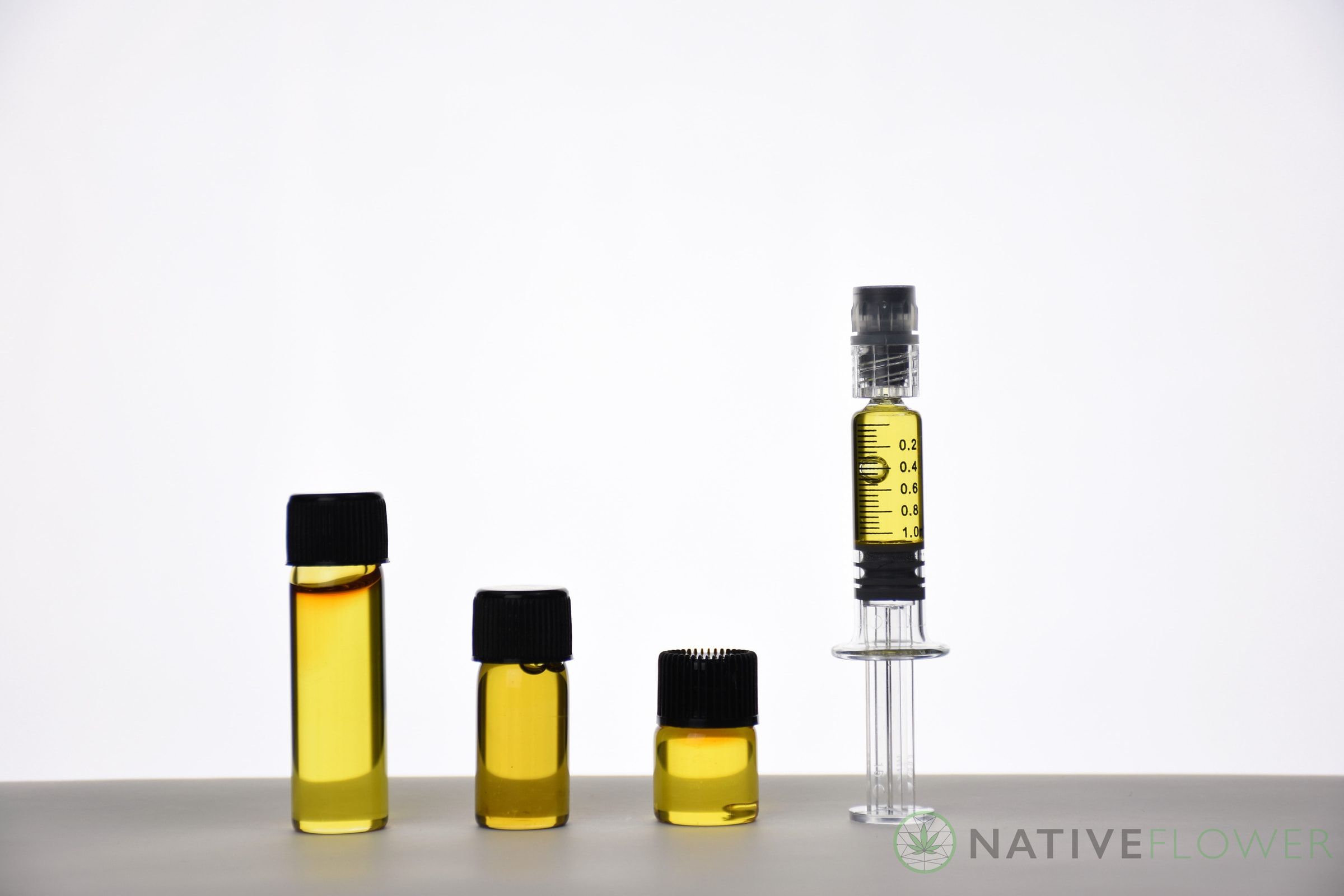 Three glass vials of golden distillate in descending sizes beside a graduated glass applicator.
