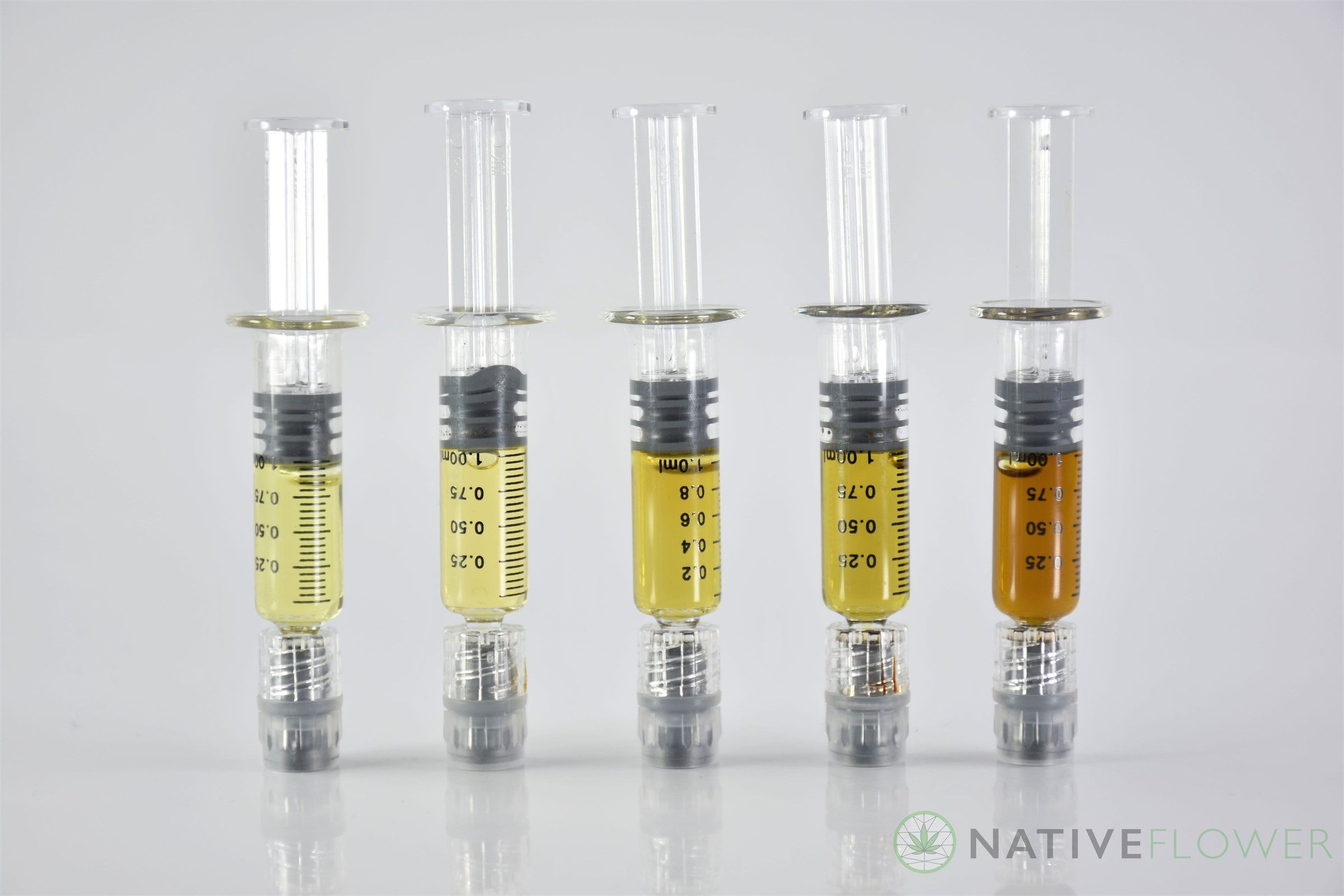 Five glass applicators of distillate in a row, four pale gold and one amber.
