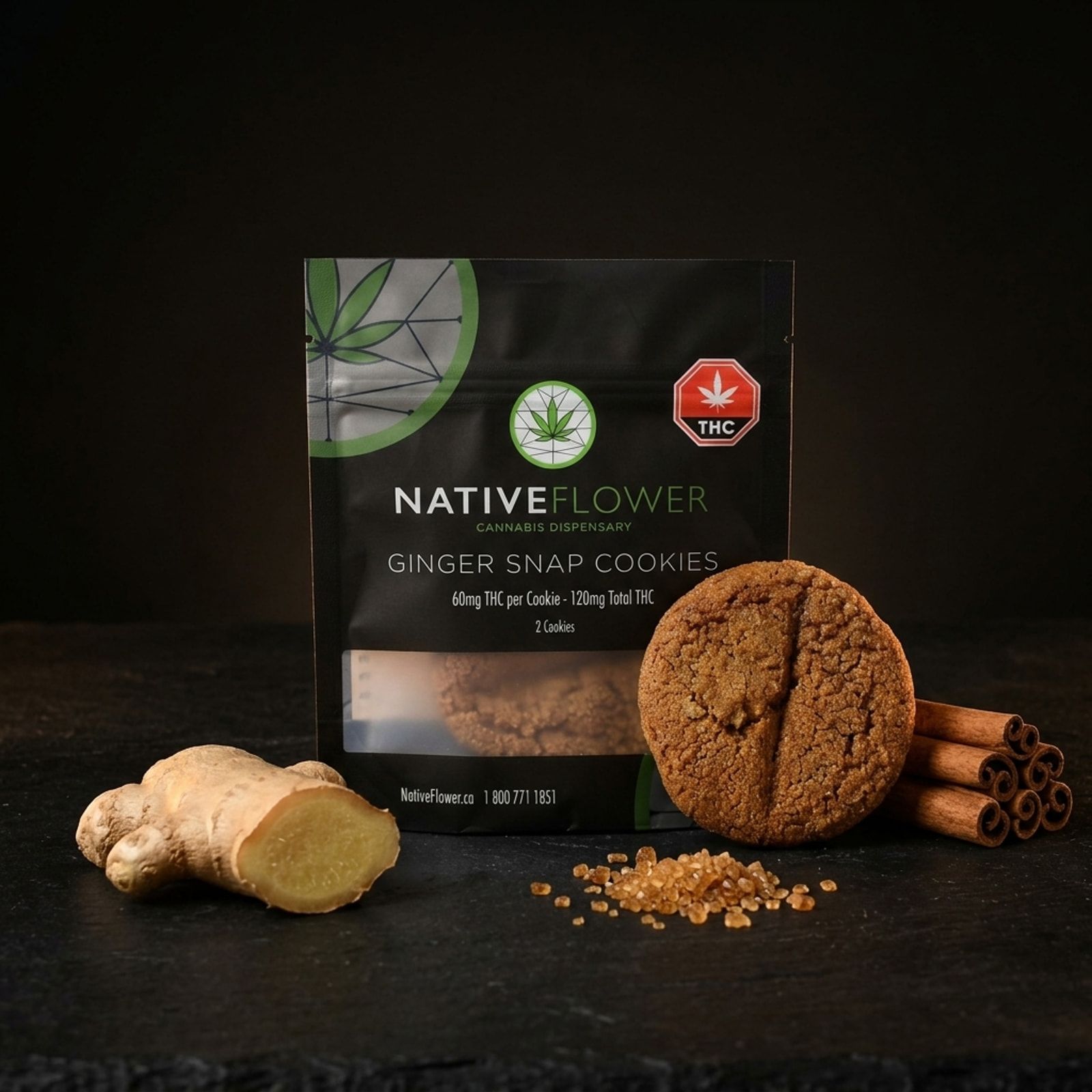 A ginger snap cookie leaning against its black Native Flower pouch on slate, with fresh ginger root, raw sugar crystals and cinnamon sticks.