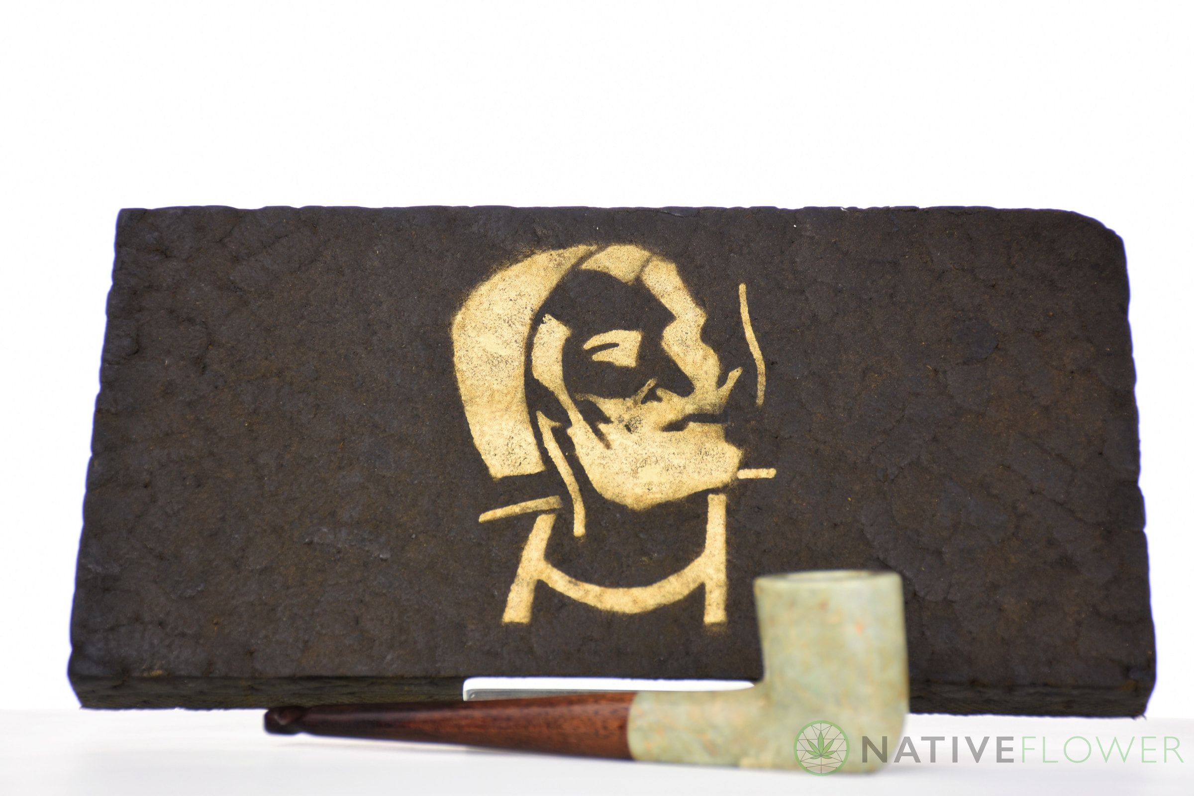 A large pressed hash slab stamped with a gold stencil, a stone pipe resting in front of it.