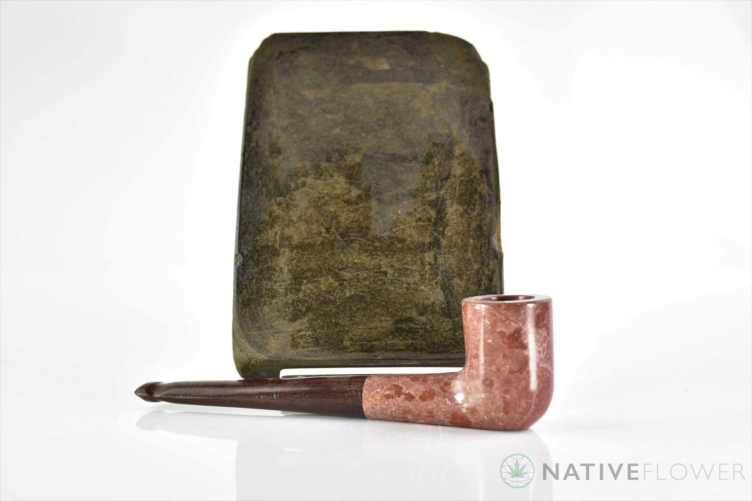A pressed slab of Gold Seal hash standing behind a wooden pipe.