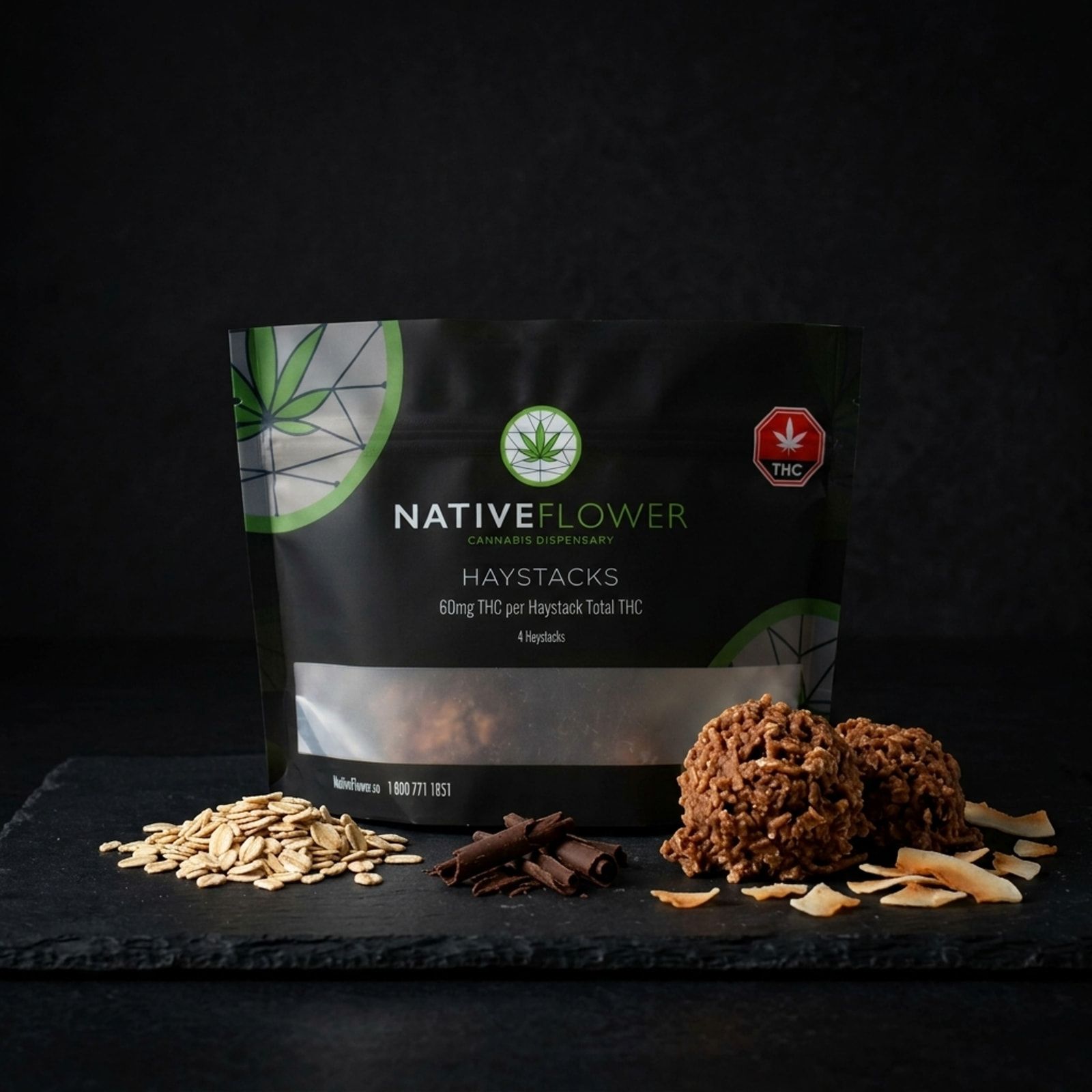 Two chocolate coconut haystacks beside their black Native Flower pouch on slate, with rolled oats, chocolate curls and toasted coconut flakes.