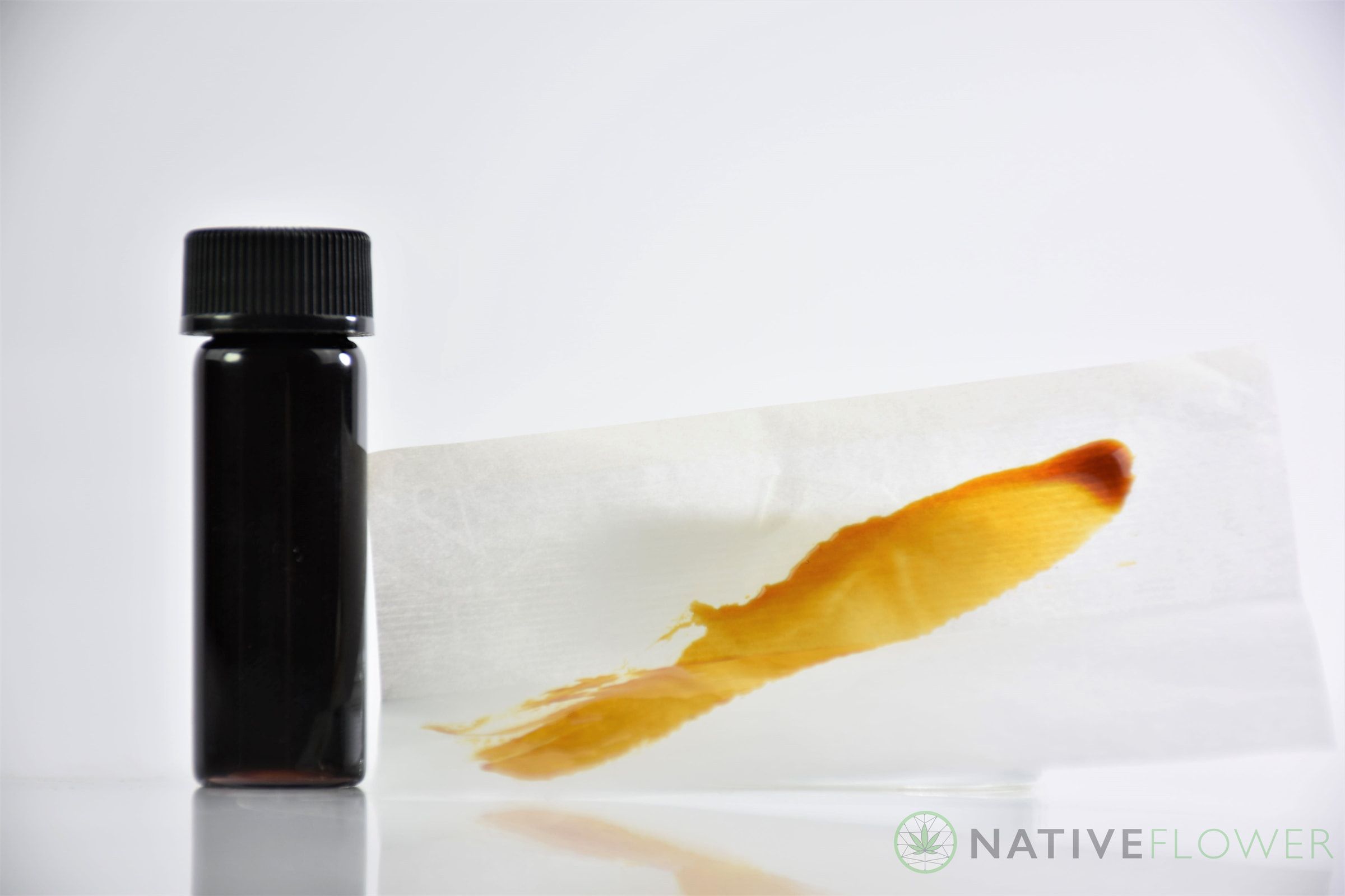 A small black bottle beside a smear of amber oil on parchment paper.