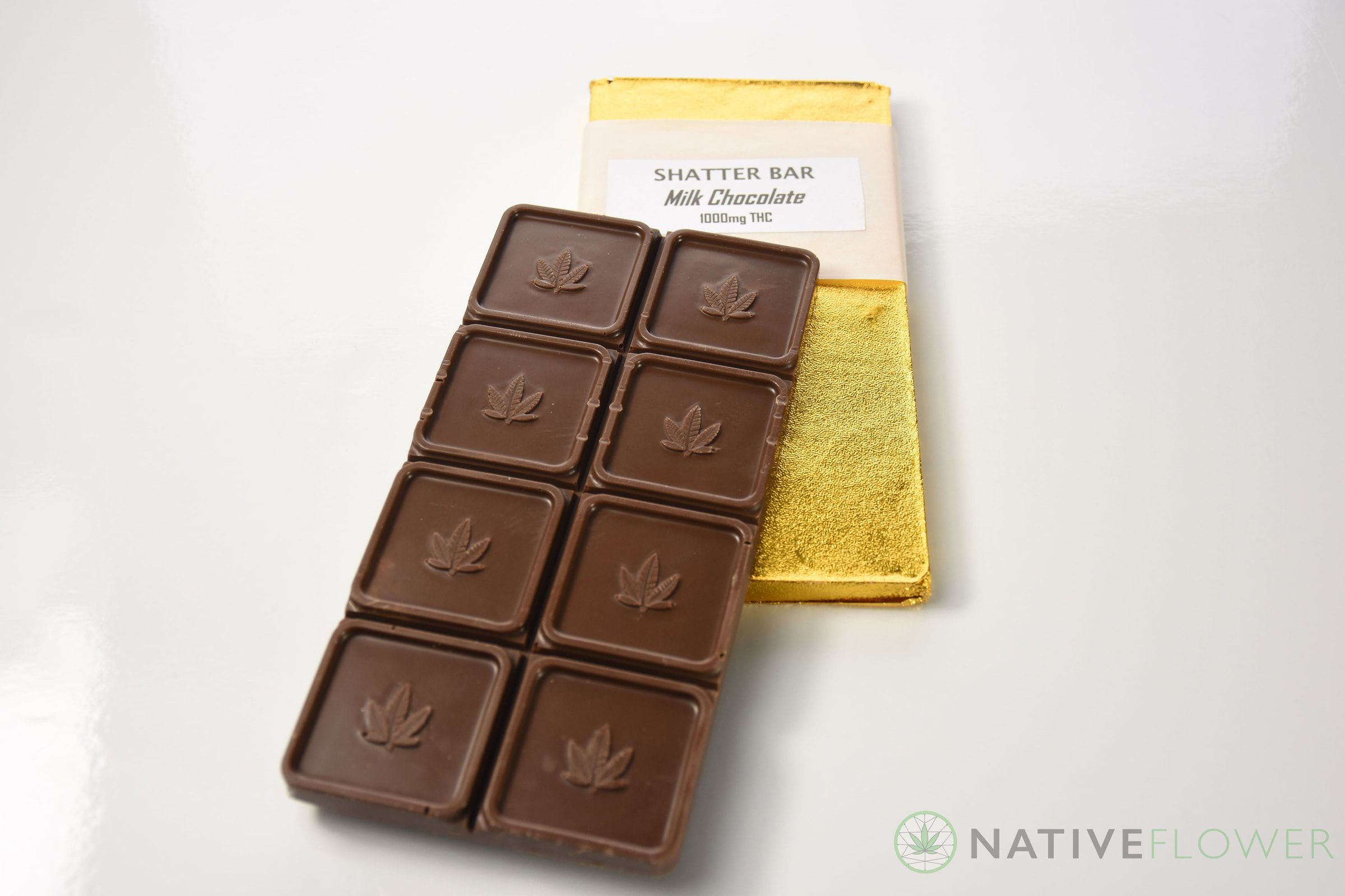 A milk chocolate bar of leaf-embossed squares lying on its opened gold wrapper.