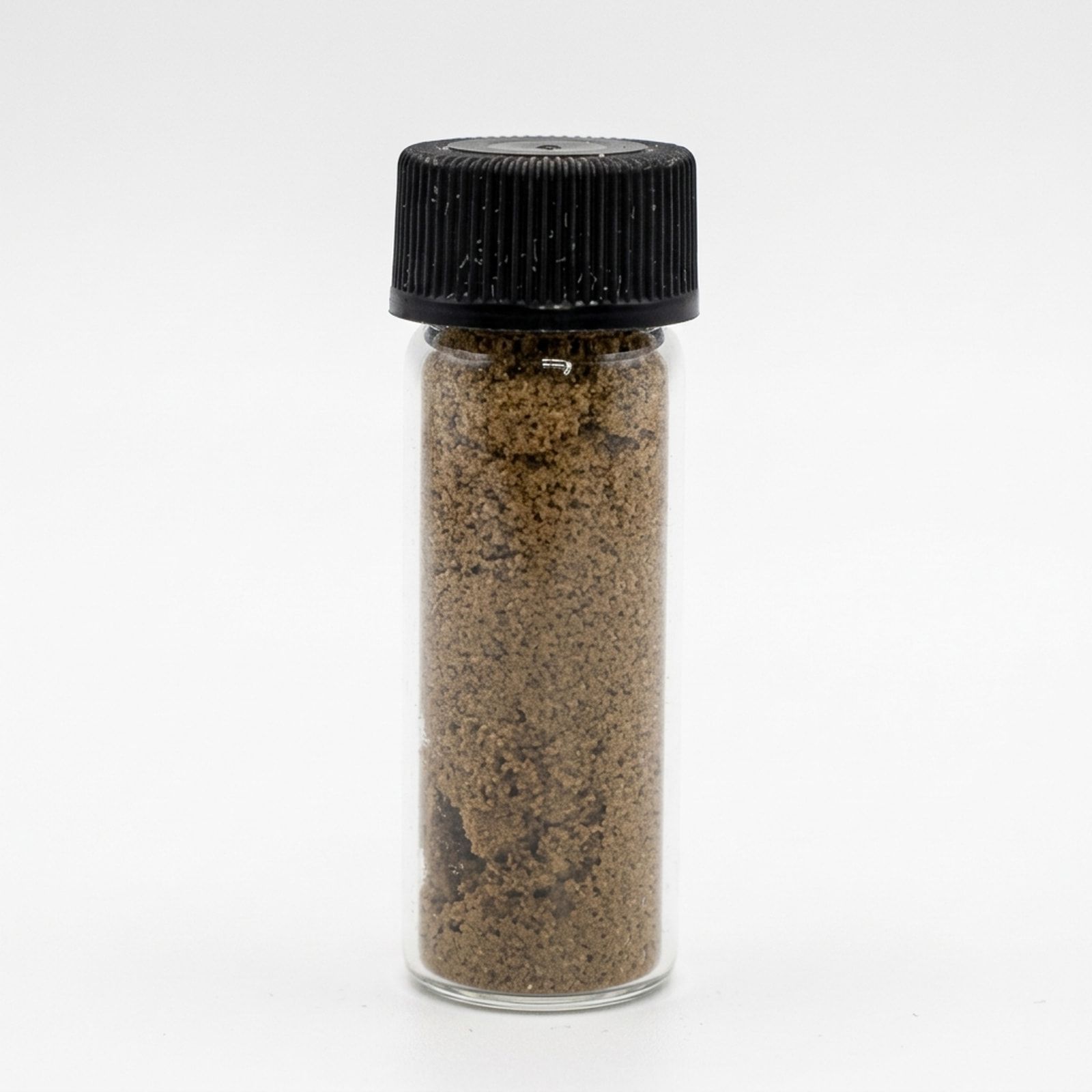 A clear glass vial with a black screw cap, packed with light brown kief, on a white background.