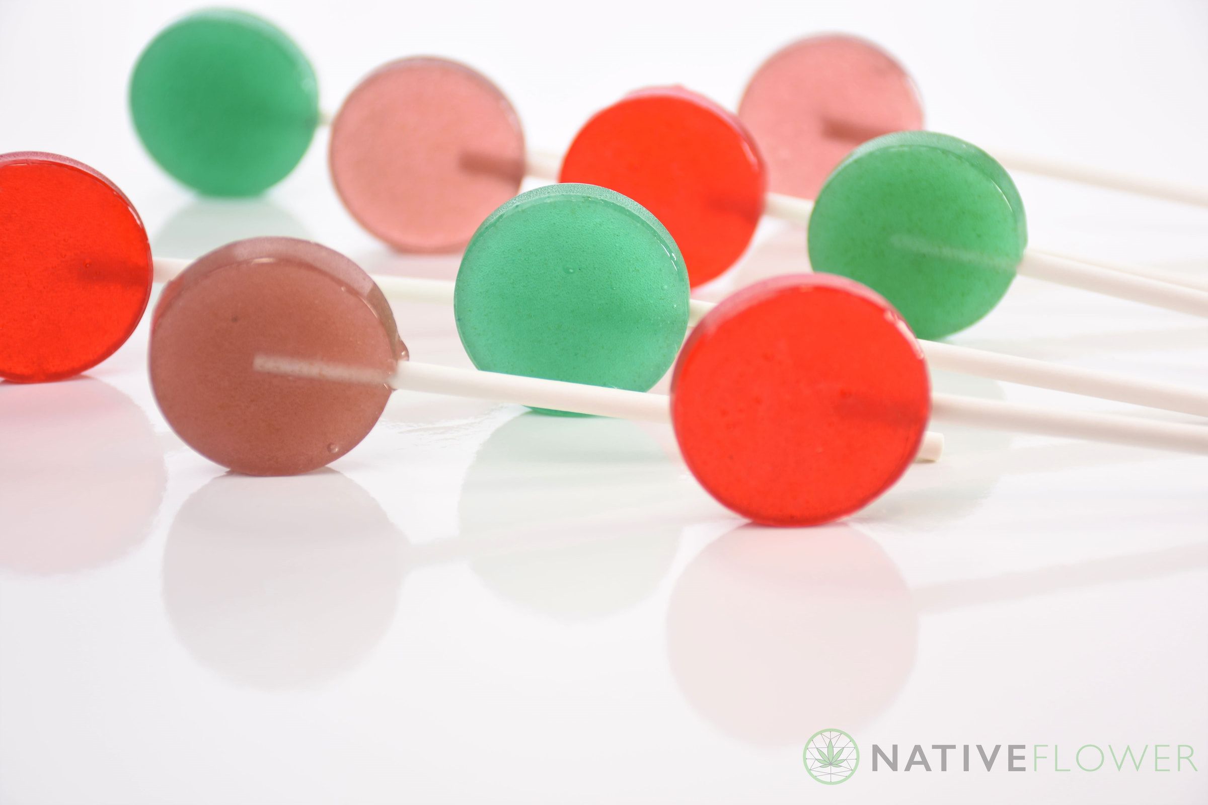 Eight unwrapped lollipops in green, red, pink and brown, lying on their sticks.