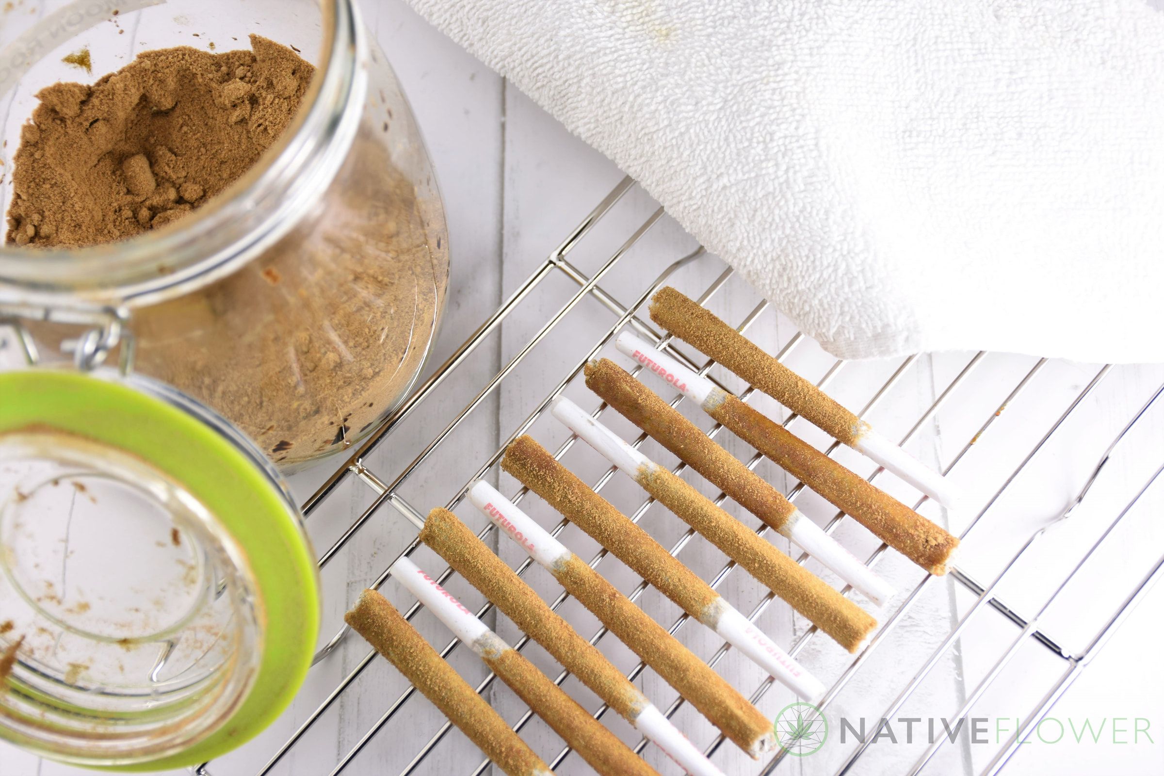 Freshly coated spliffs resting on a wire rack beside an open jar of kief.