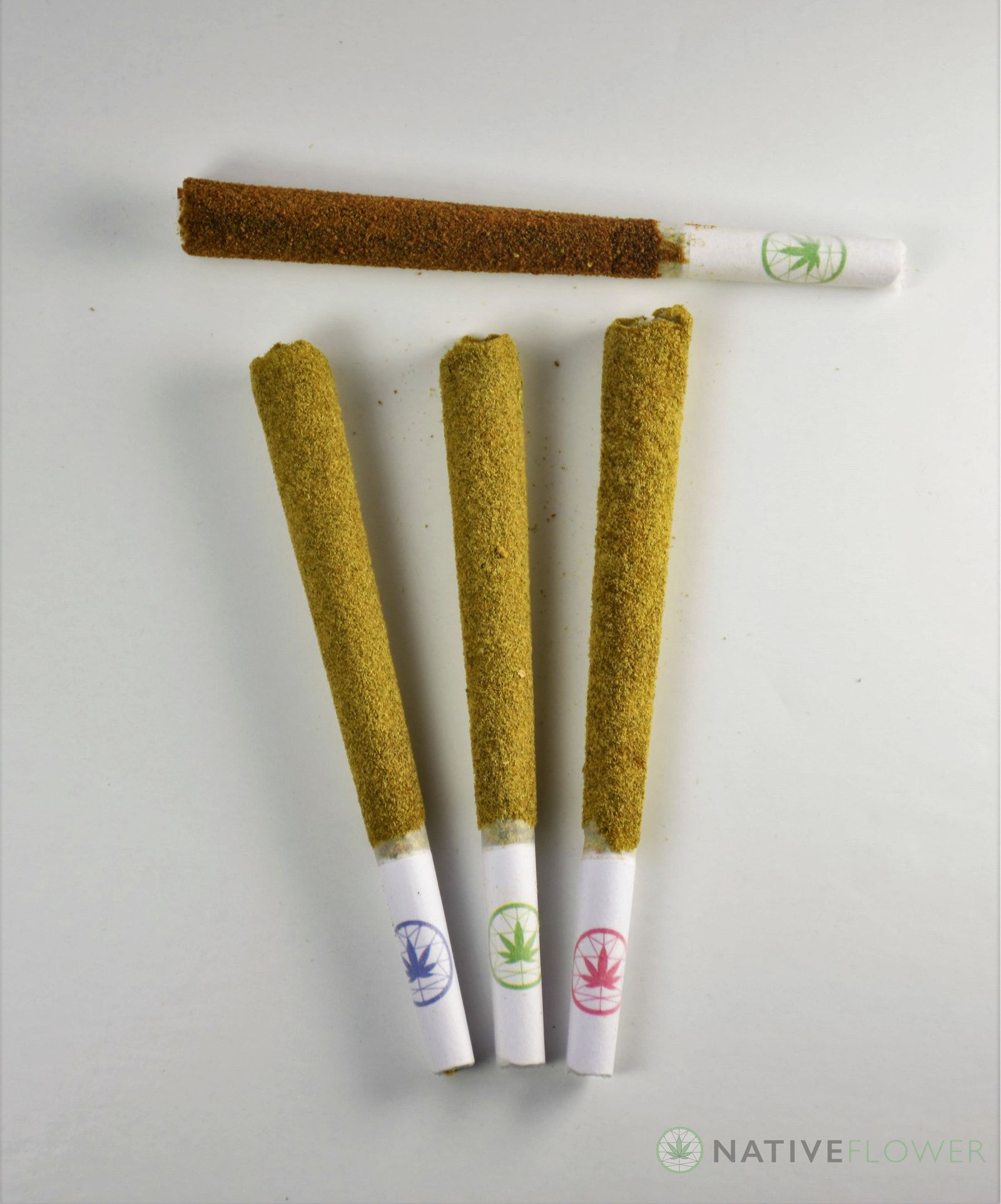 Four kief-coated spliffs arranged on a pale surface, seen from above.