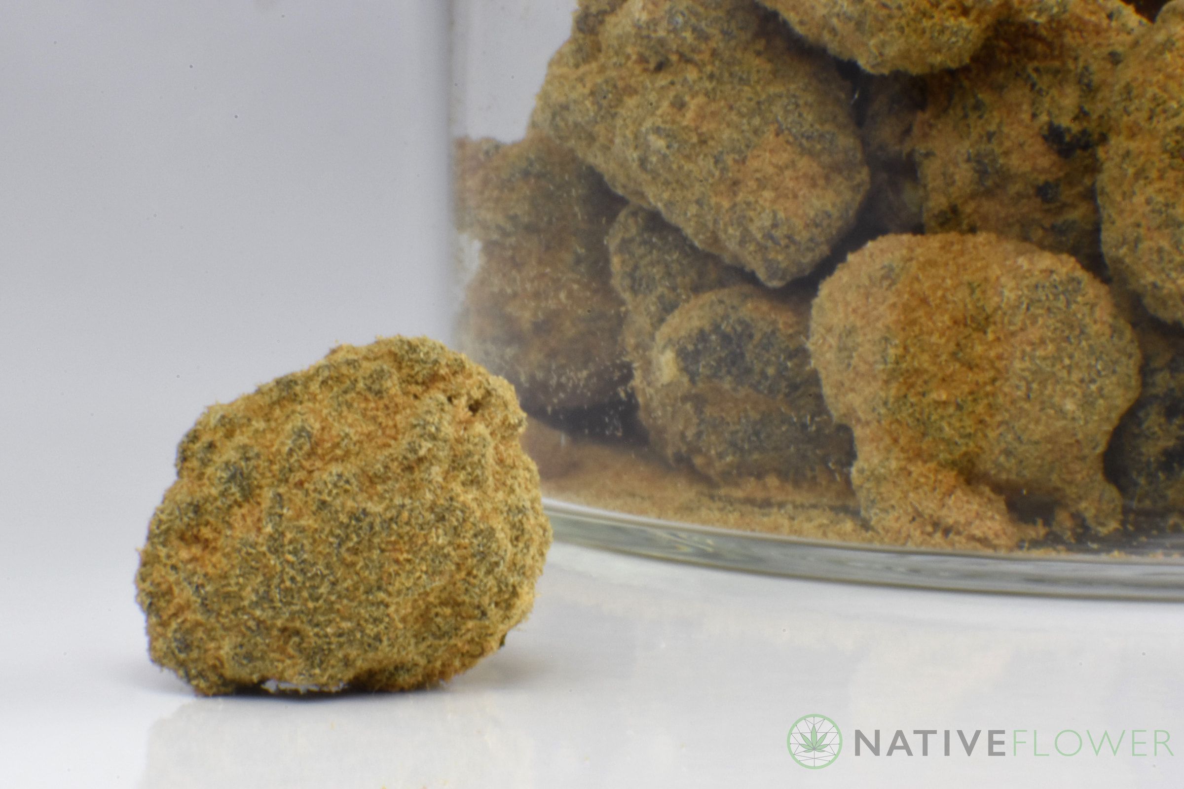 A single kief-coated bud in front of a glass jar packed with more.