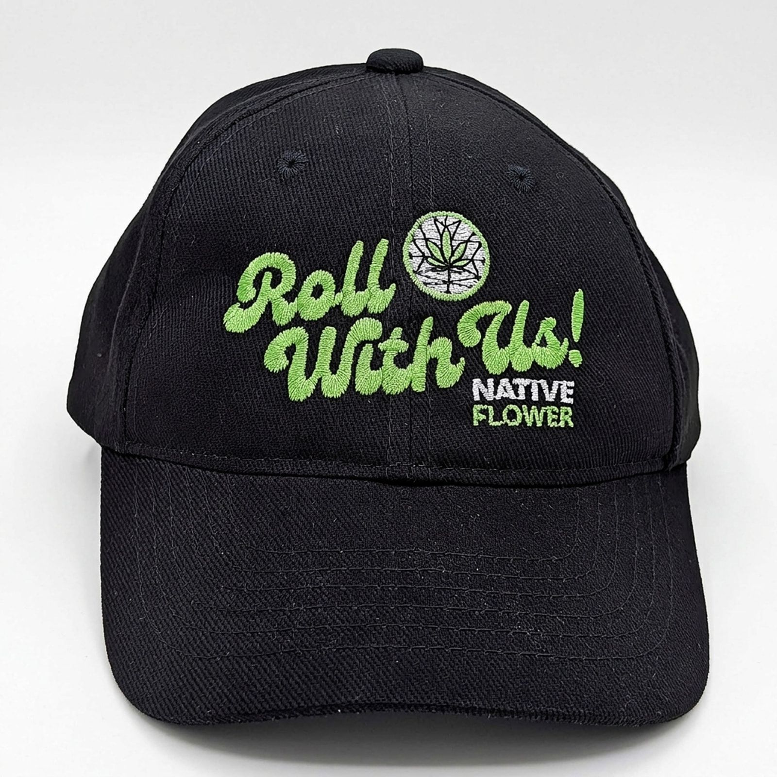 A black Native Flower ball cap facing forward, Roll With Us embroidered in green beside the Native Flower logo, on a white background.