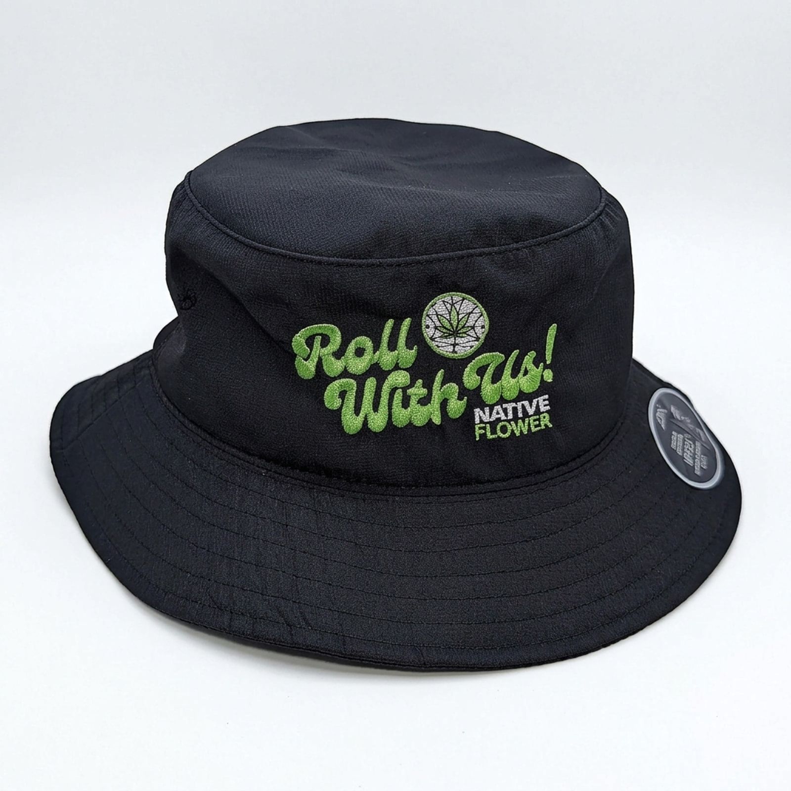 A black Native Flower bucket hat with Roll With Us embroidered in green beside the Native Flower logo, on a white background.