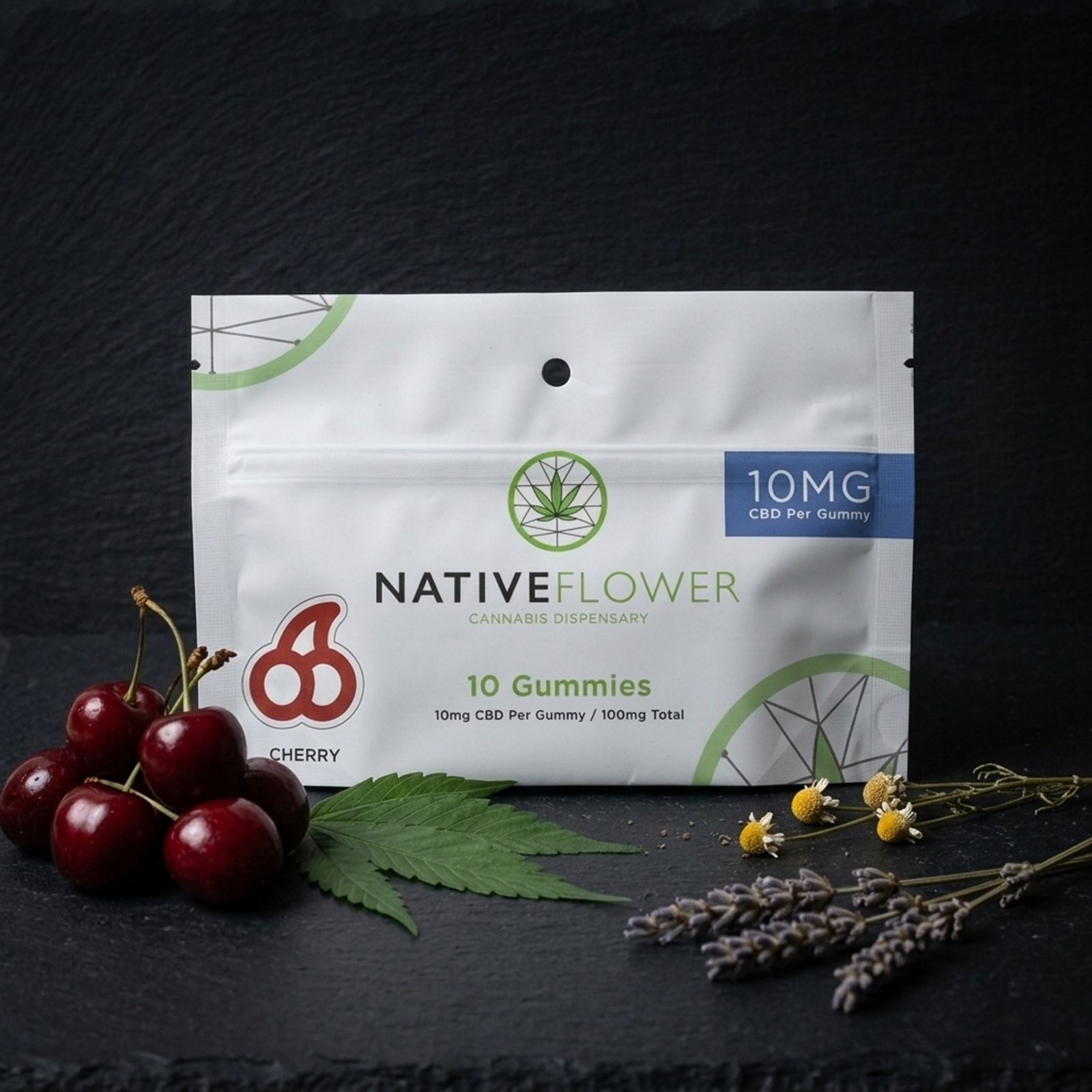 A white Native Flower cherry CBD gummies pouch on slate, fresh cherries and a cannabis leaf on one side, chamomile and lavender on the other.