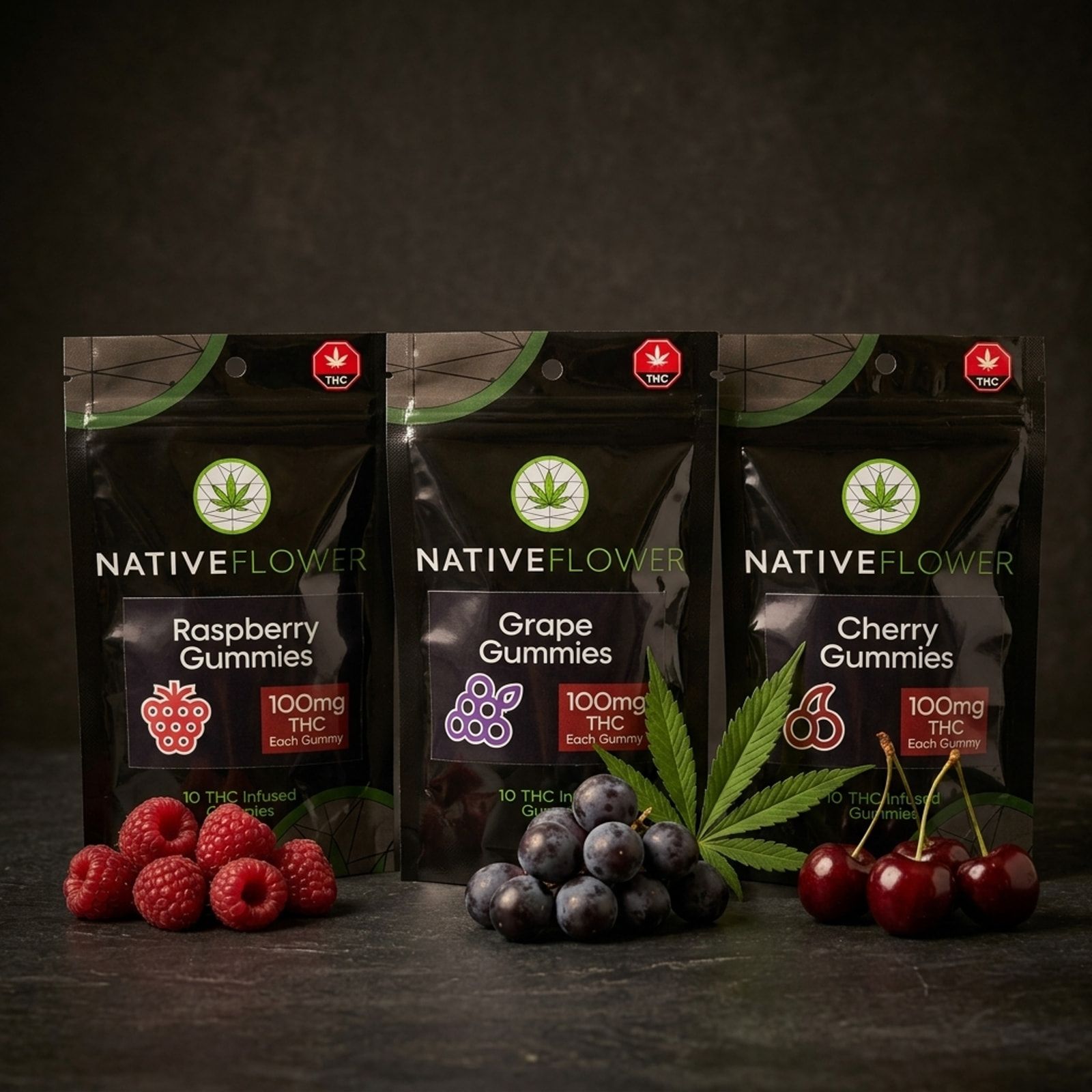 Three black Native Flower gummy pouches in a row — raspberry, grape and cherry — with fresh fruit and a cannabis leaf in front.