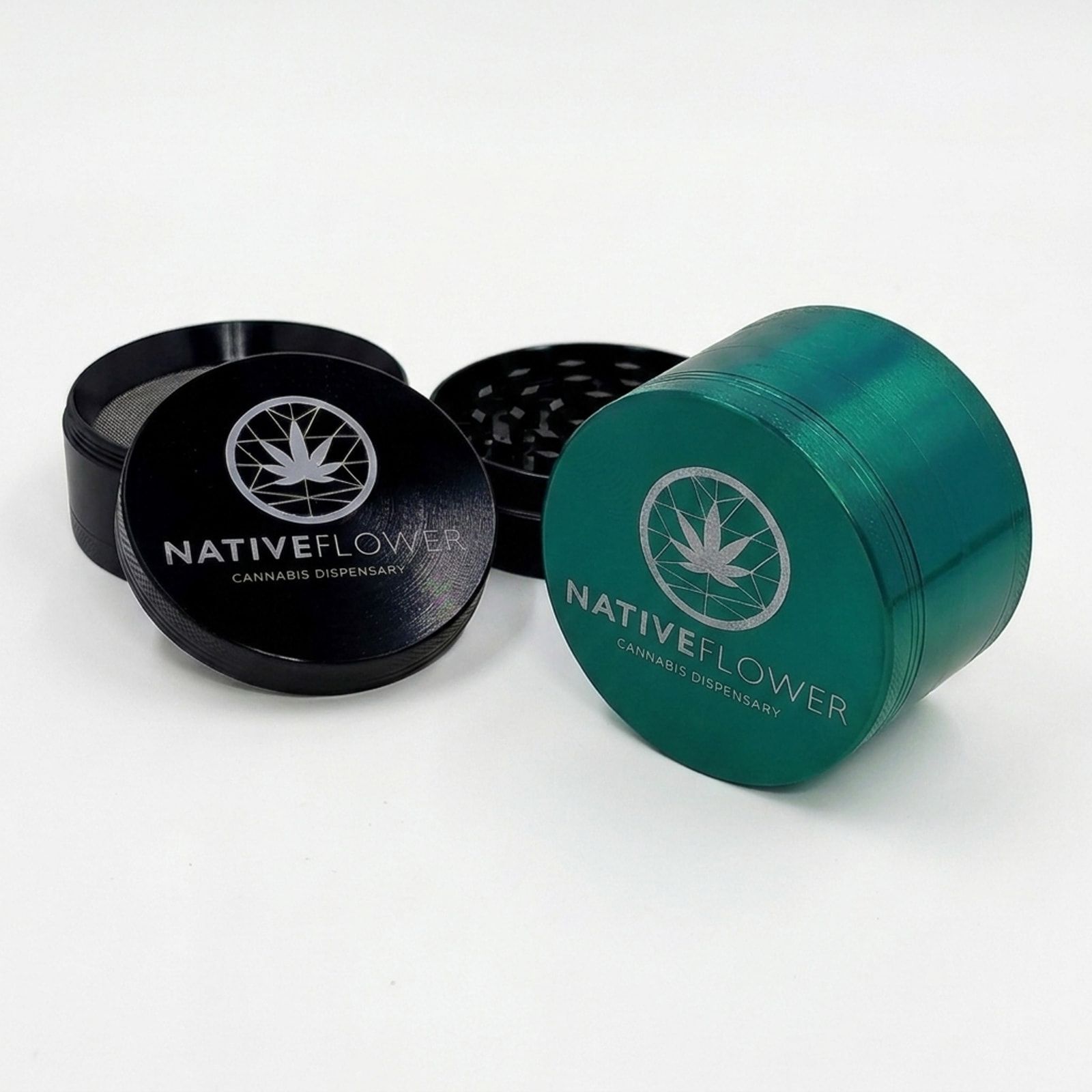 A black Native Flower metal grinder opened to show its teeth and screen beside a closed green one, on a white background.