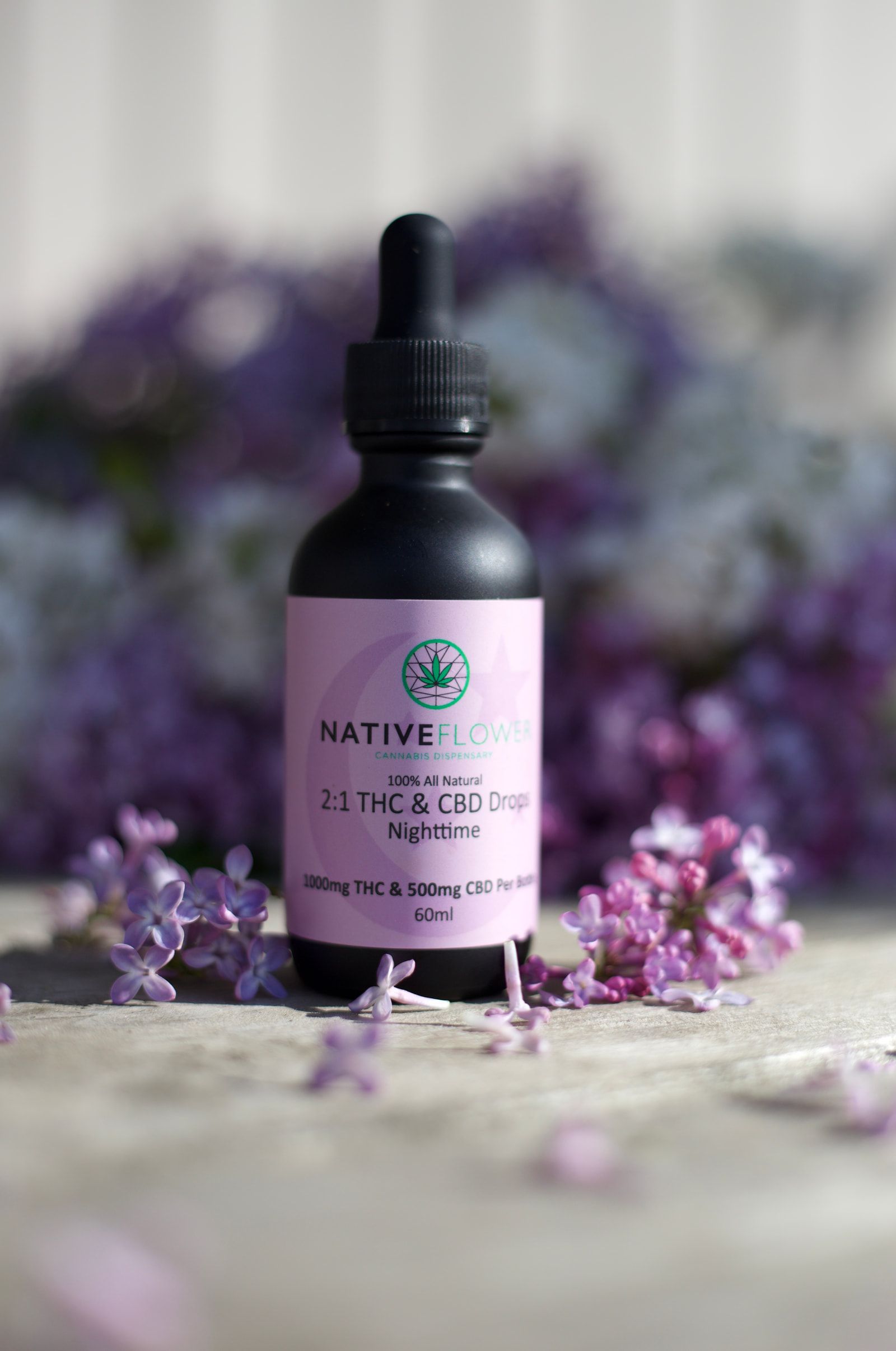 The nighttime bottle standing on stone among scattered lilac blossom.
