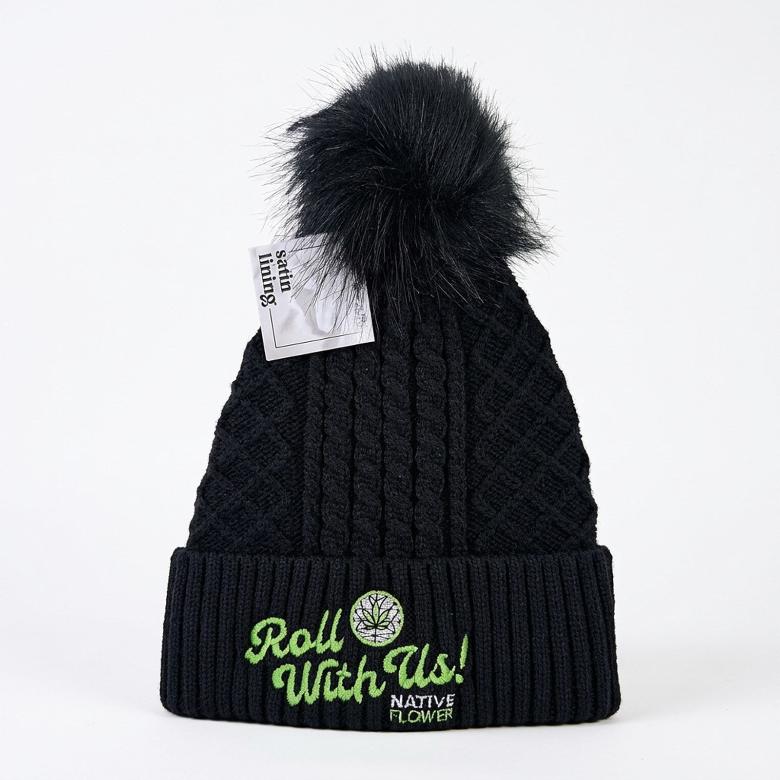 A black cable-knit Native Flower toque with a black pom pom on a white background, Roll With Us embroidered in green on the cuff.