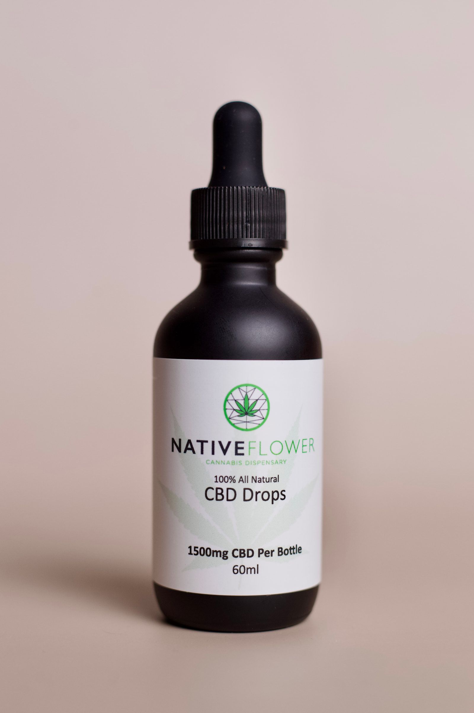 A bottle of Native Flower CBD drops photographed against a warm grey background.