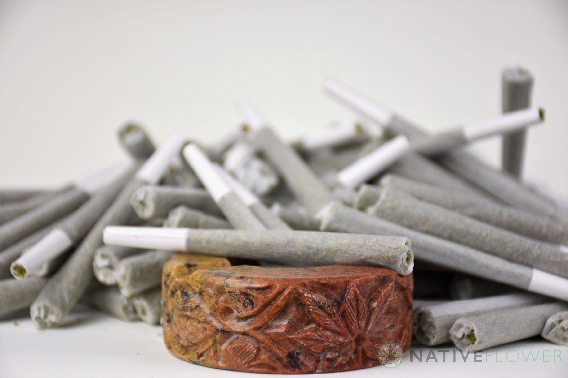 A loose pile of Native Flower pre-rolled joints beside a carved wooden ring.