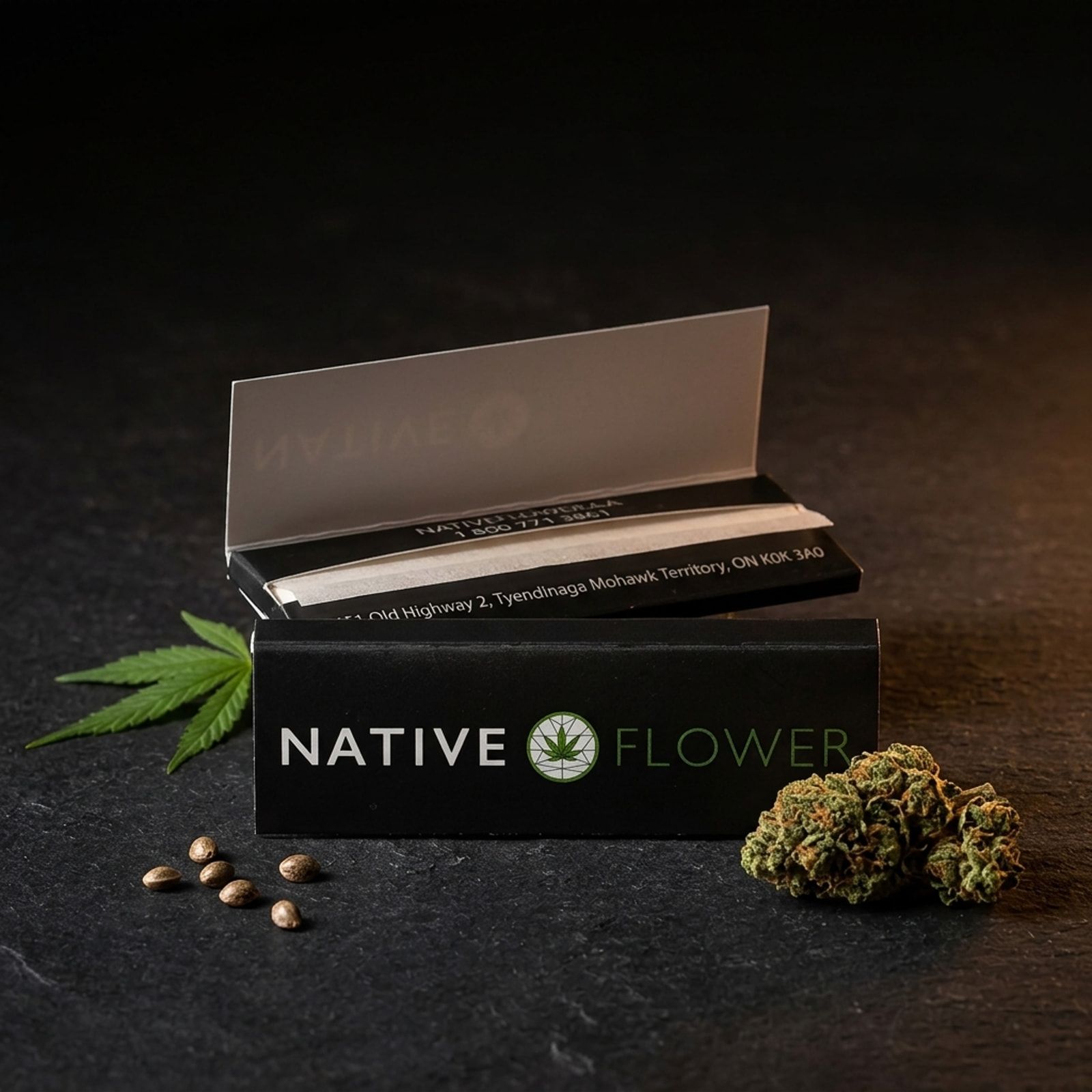 An open black booklet of Native Flower rolling papers on dark slate, with a cannabis leaf, a few seeds and a dried bud beside it.