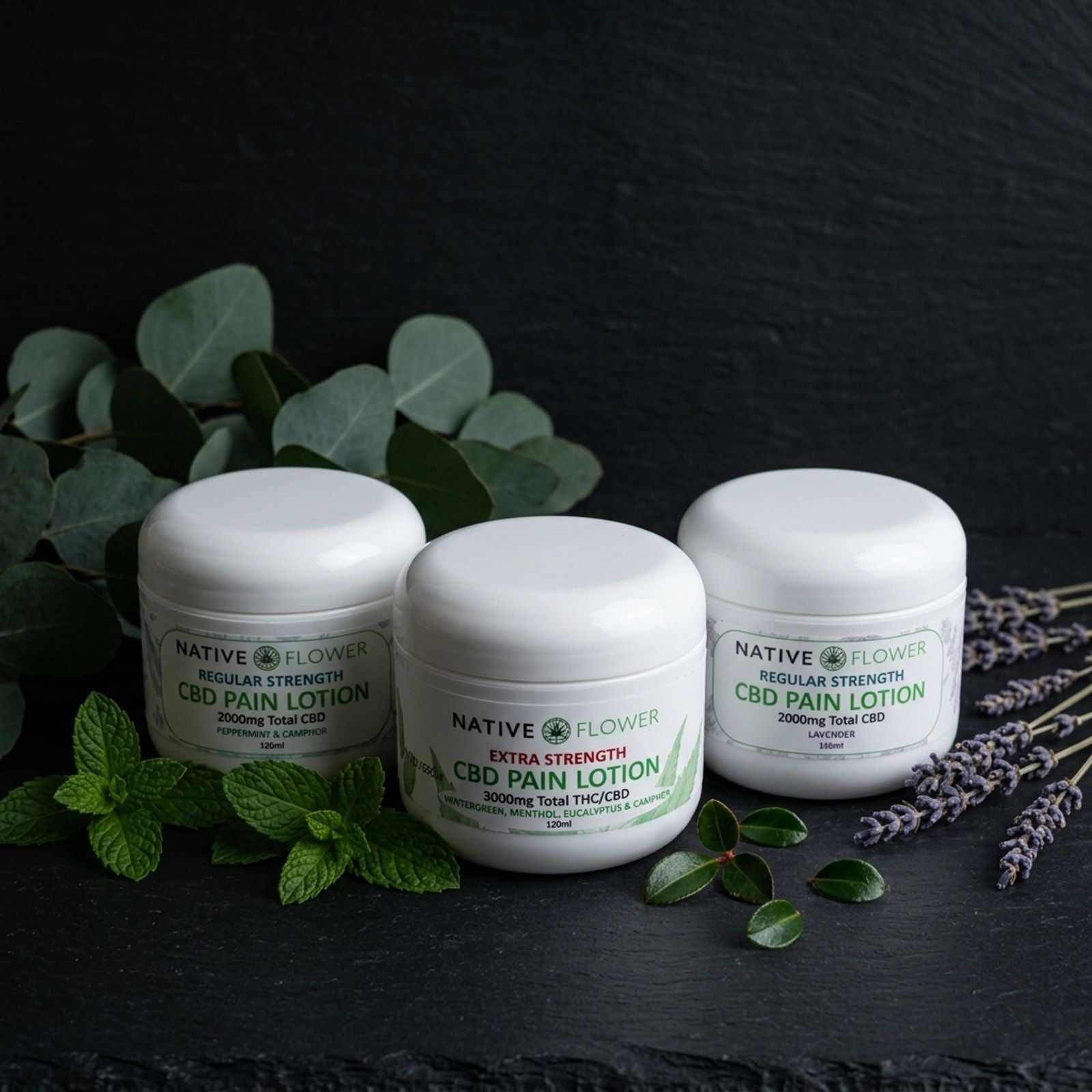 Three white Native Flower topical lotion jars on slate, surrounded by eucalyptus, fresh mint, small green leaves and lavender sprigs.
