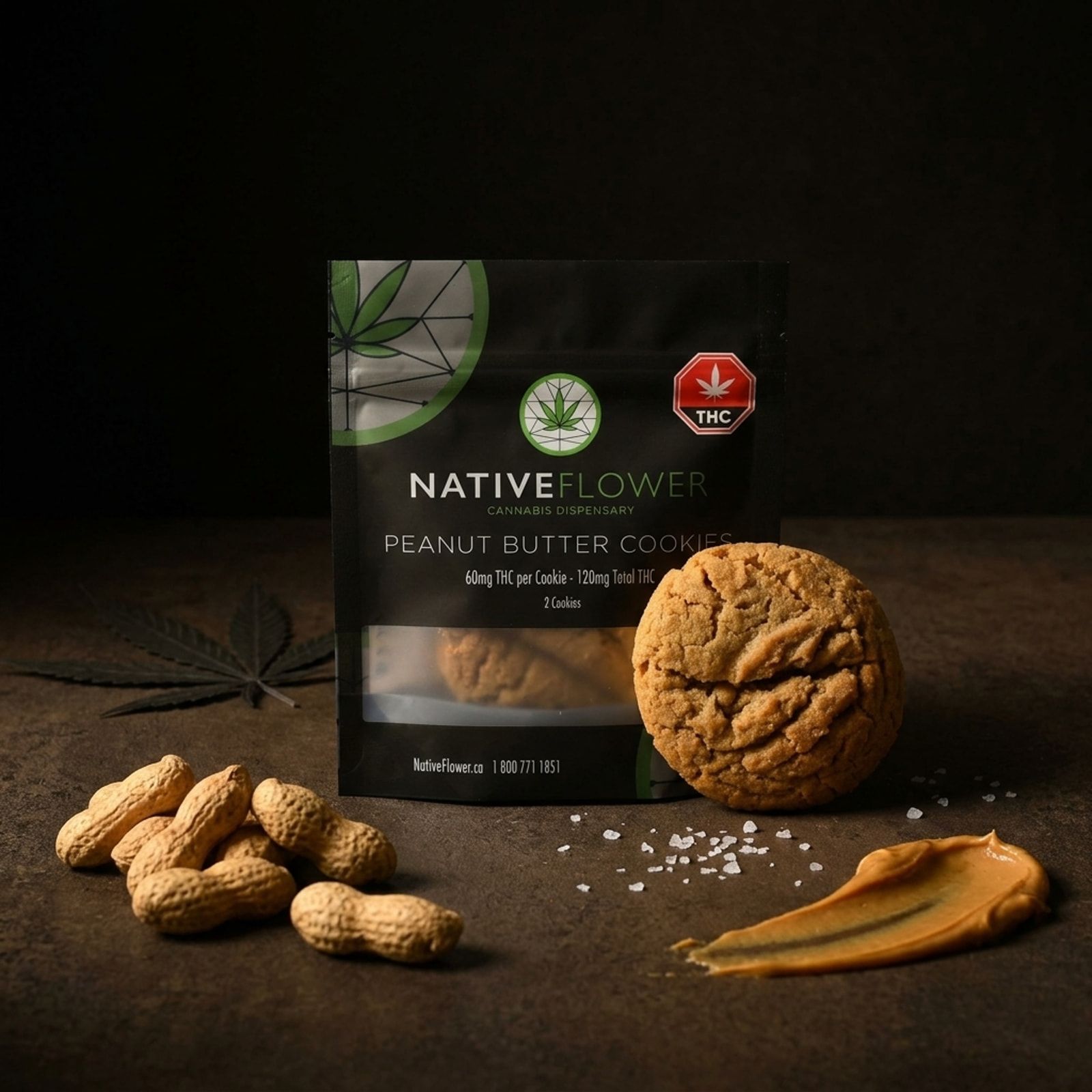 A Native Flower peanut butter cookie leaning against its black pouch, with whole peanuts, a smear of peanut butter and flaky salt.