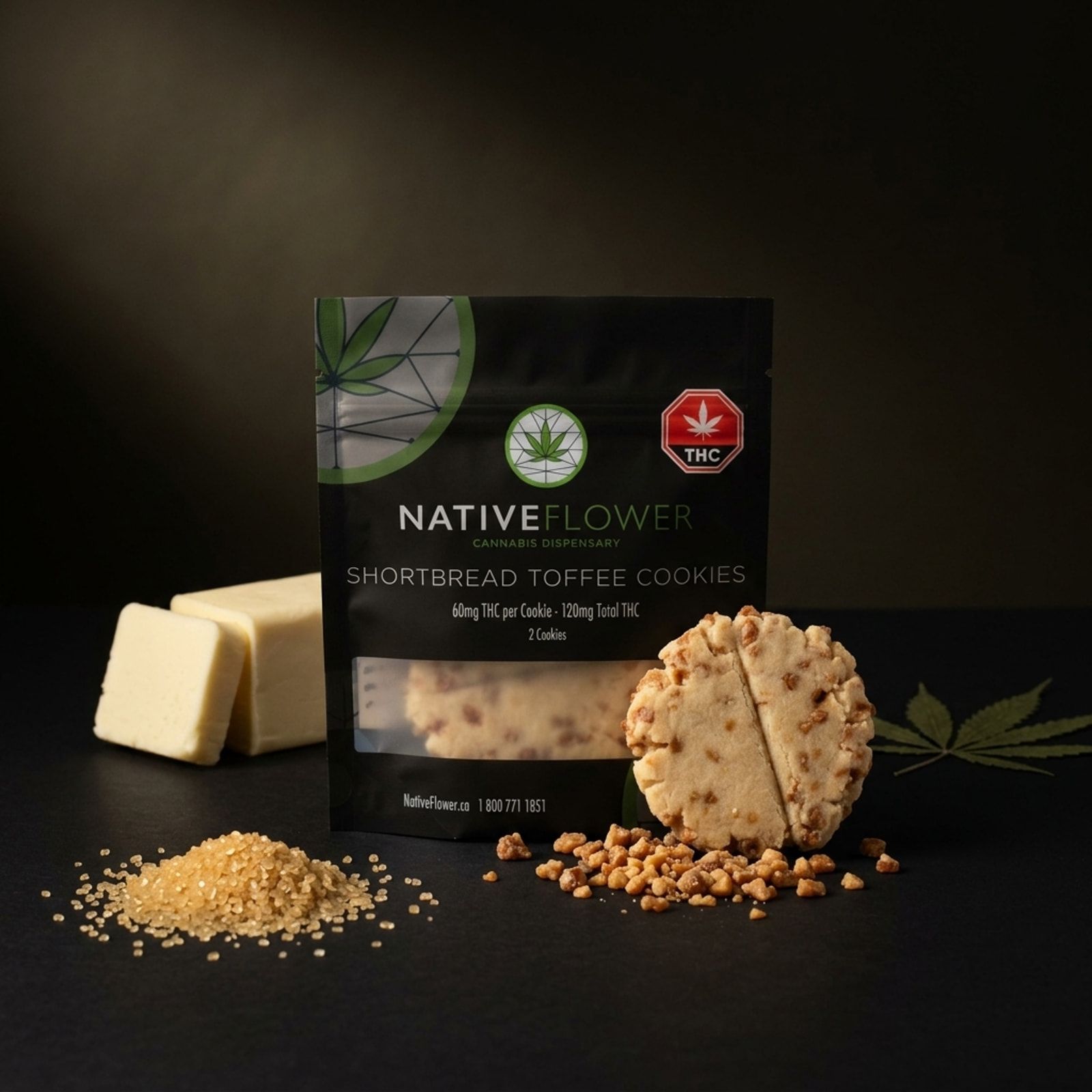 A Native Flower shortbread toffee cookie, scored in half, leaning on its black pouch beside butter, raw sugar, toffee bits and a cannabis leaf.