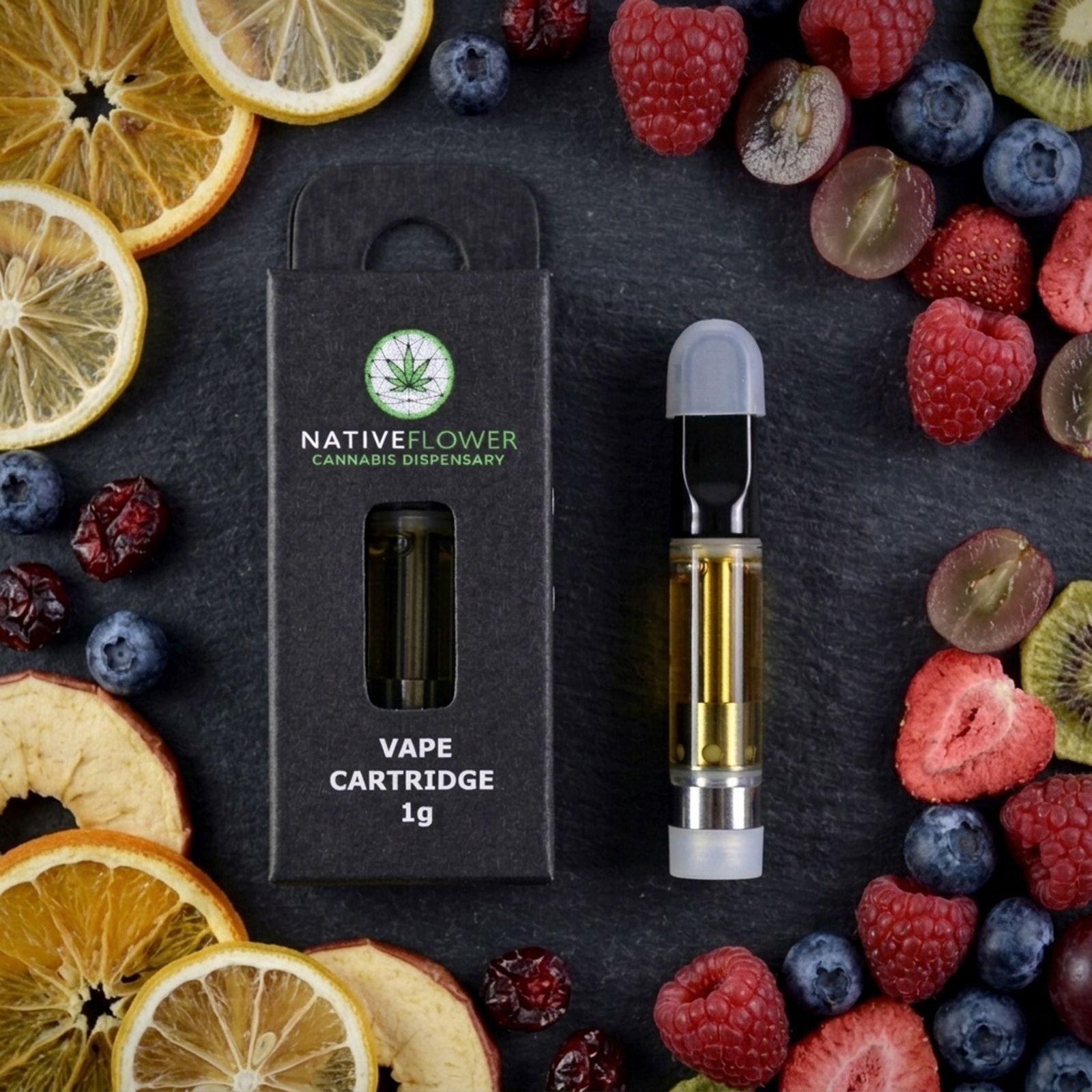 A black Native Flower vape cartridge box and an amber-filled cartridge seen from above on slate, ringed by dried citrus slices, berries, grapes and kiwi.