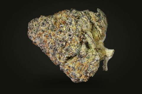 A cured bud of Zoap, olive and tan with dark purple flecks under a frost, with a leaf tip at its right, on a plain black background.